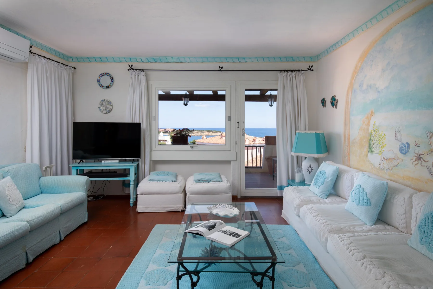 Una sala luminosa tiene asientos, una mesa de centro de vidrio y vistas al mar.