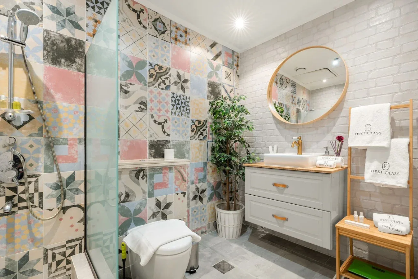 A bathroom with a glass shower, patterned tile, and a vanity.