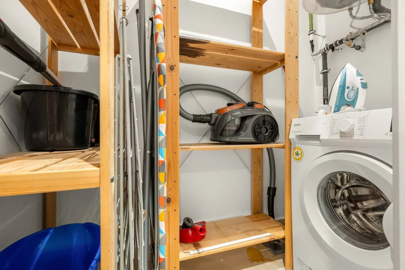 A laundry and storage area with a washing machine, vacuum, and ironing board.