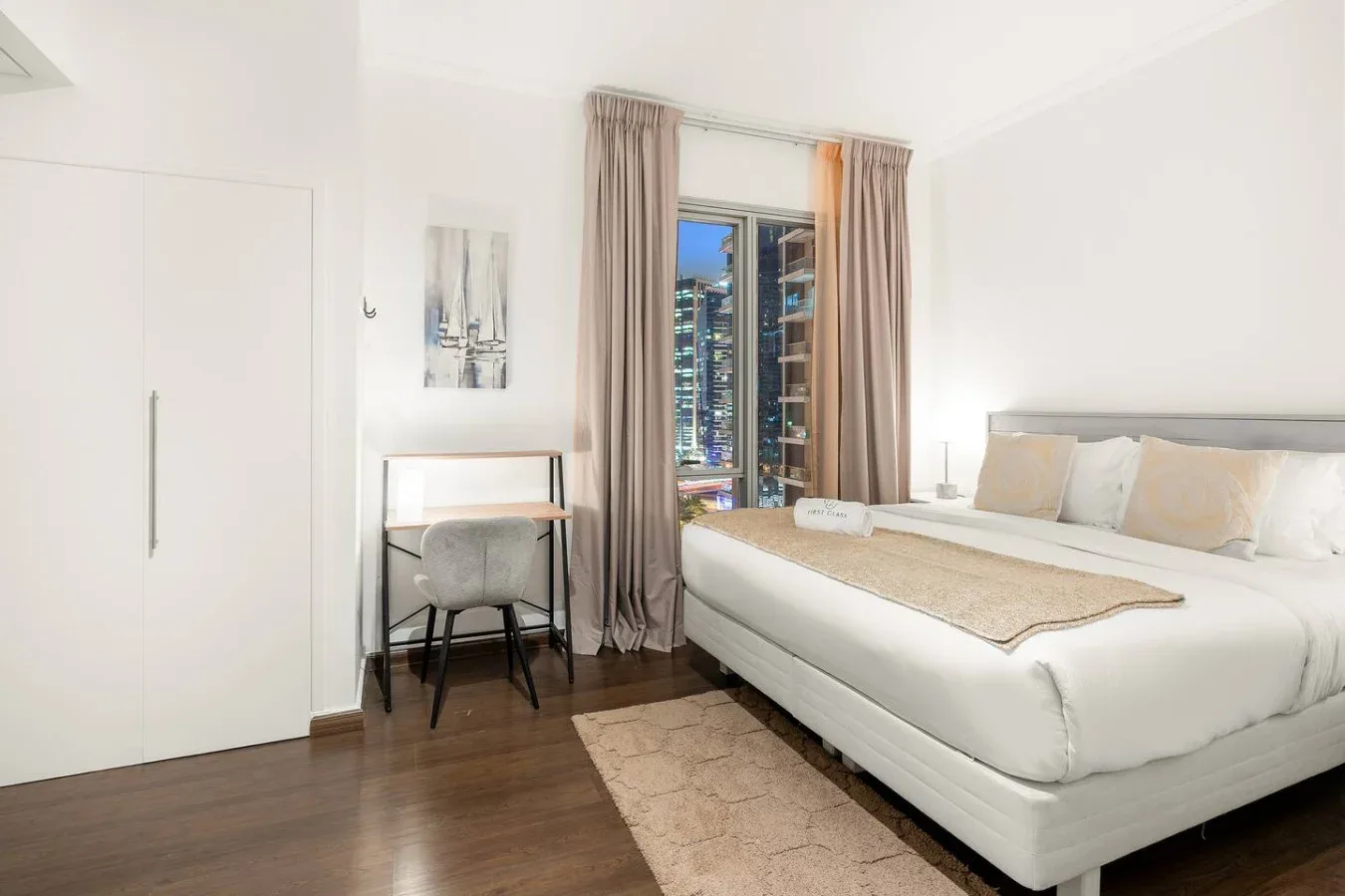 A bright bedroom with a large bed, bedside tables, and a window overlooking city buildings.