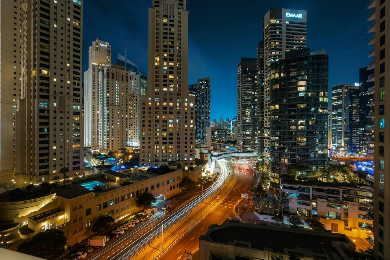 Nighttime cityscape of illuminated high-rise buildings along a busy road.