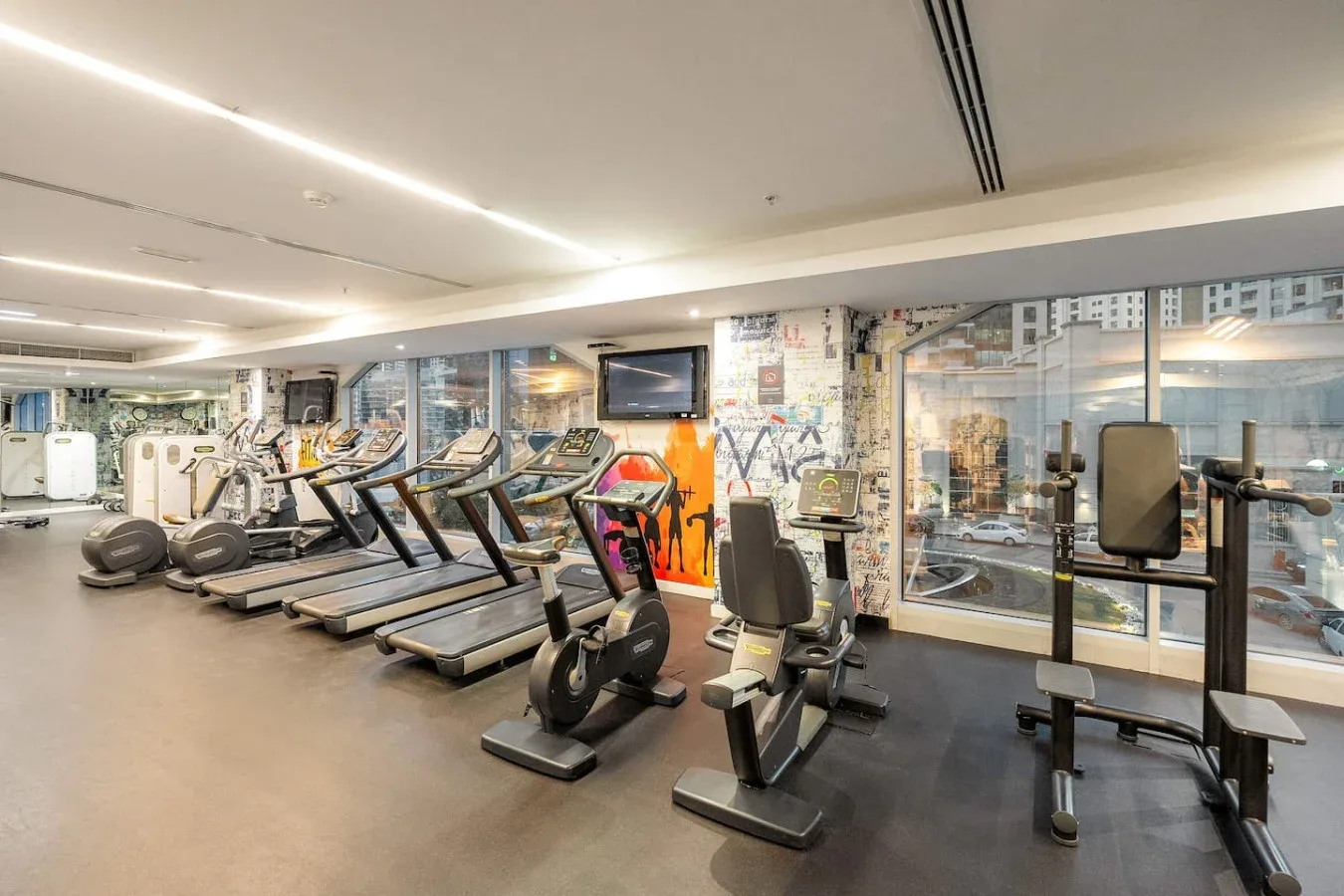 A gym with rows of treadmills and exercise bikes beside large windows.