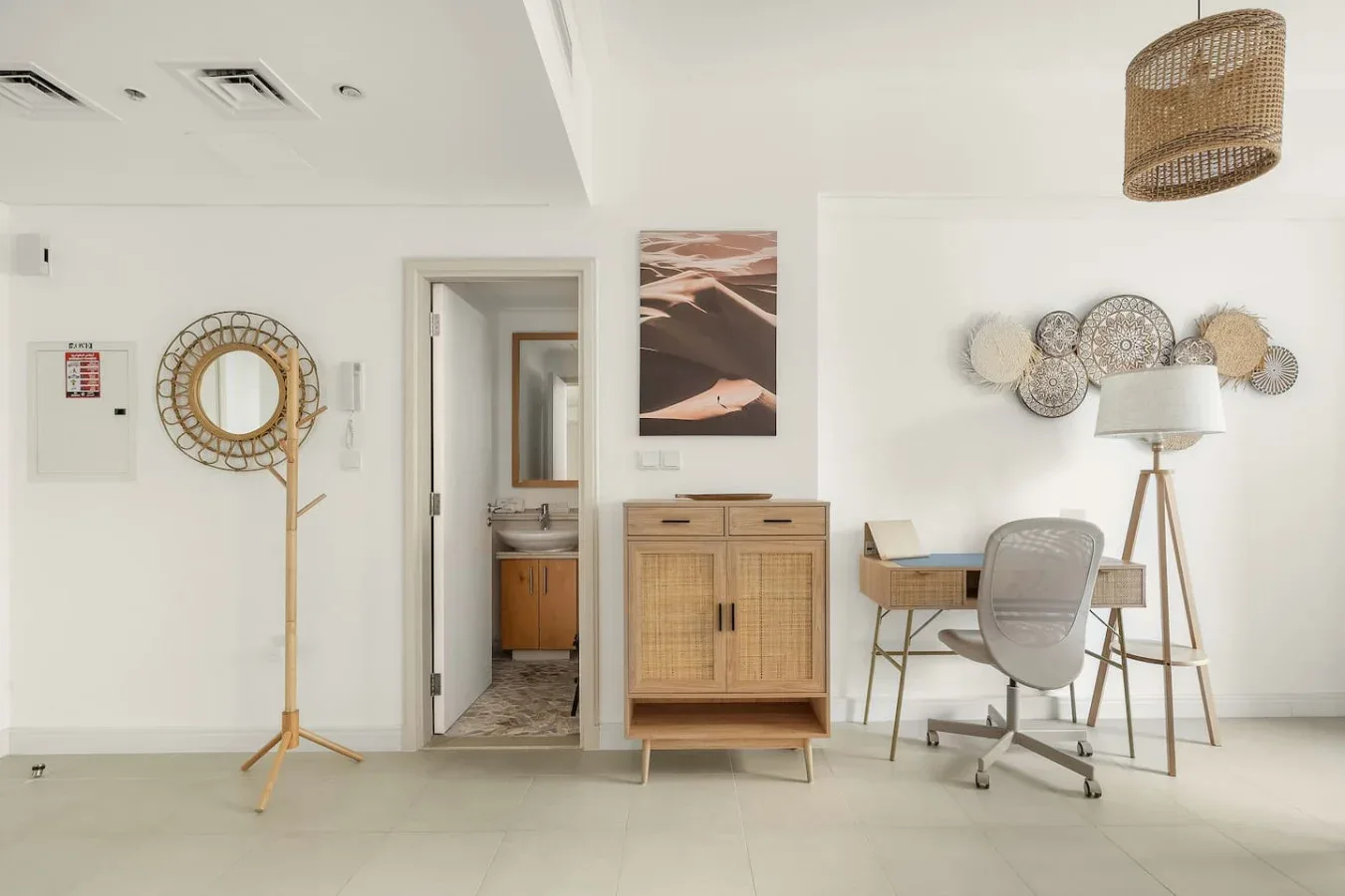 A bright room with a desk, seating, a floor lamp, and a doorway to a washroom.