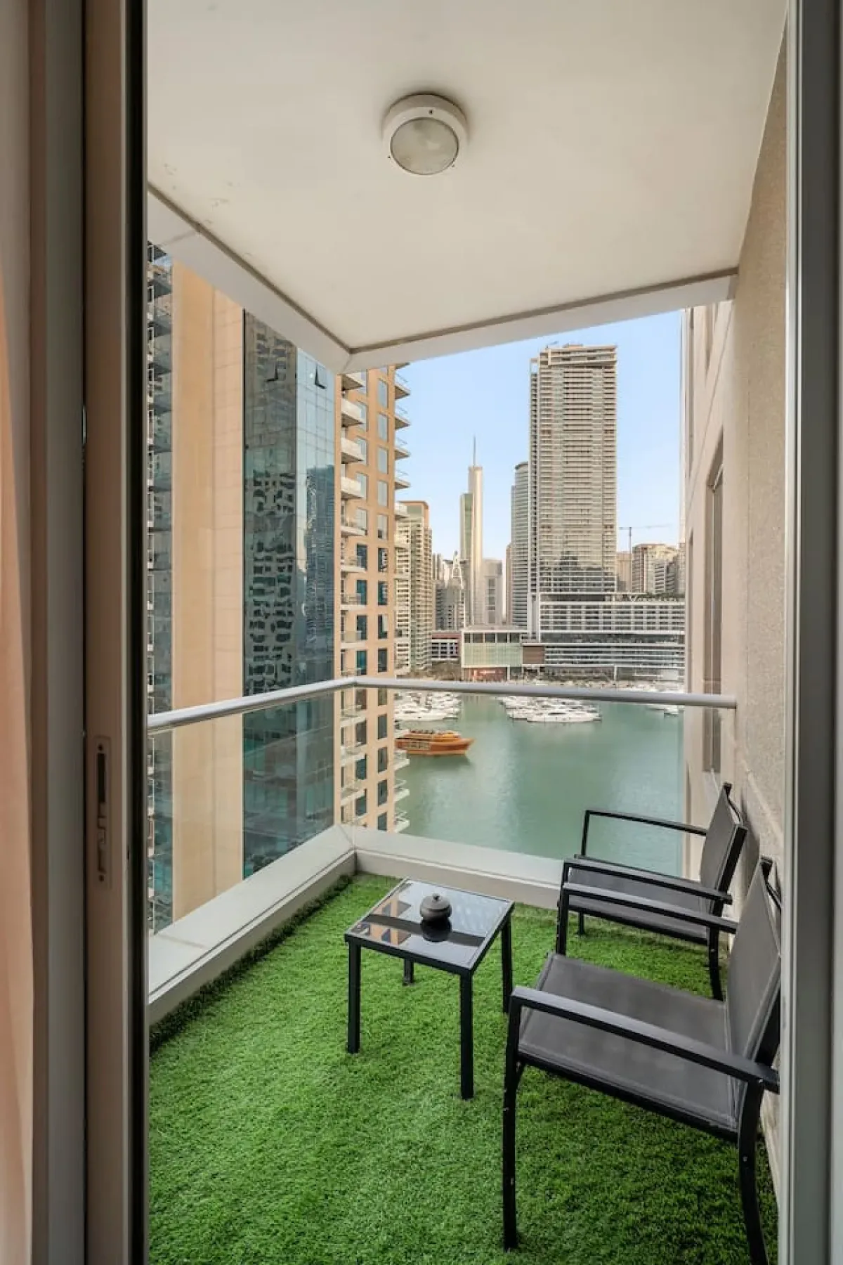 A balcony with artificial grass and seating overlooks a canal and nearby buildings.