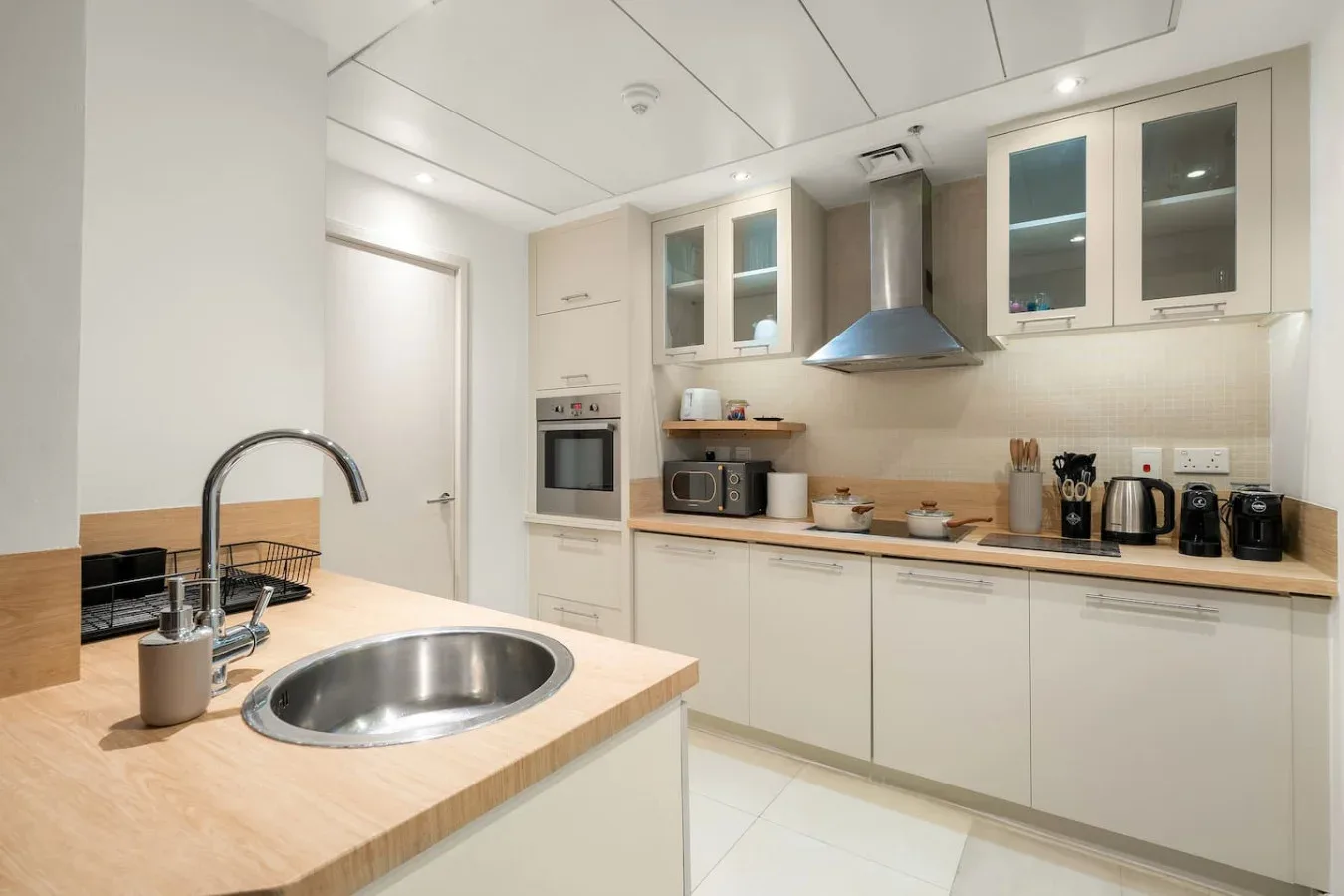 A bright kitchen with pale cabinets, a wood countertop, and a stainless-steel sink.