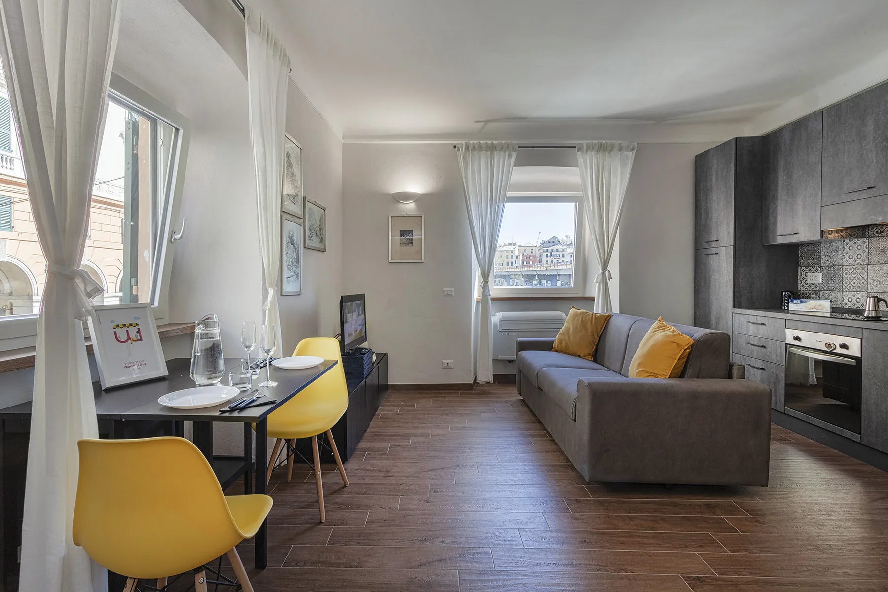 A studio living area with a gray sofa, dining table, and compact kitchen.