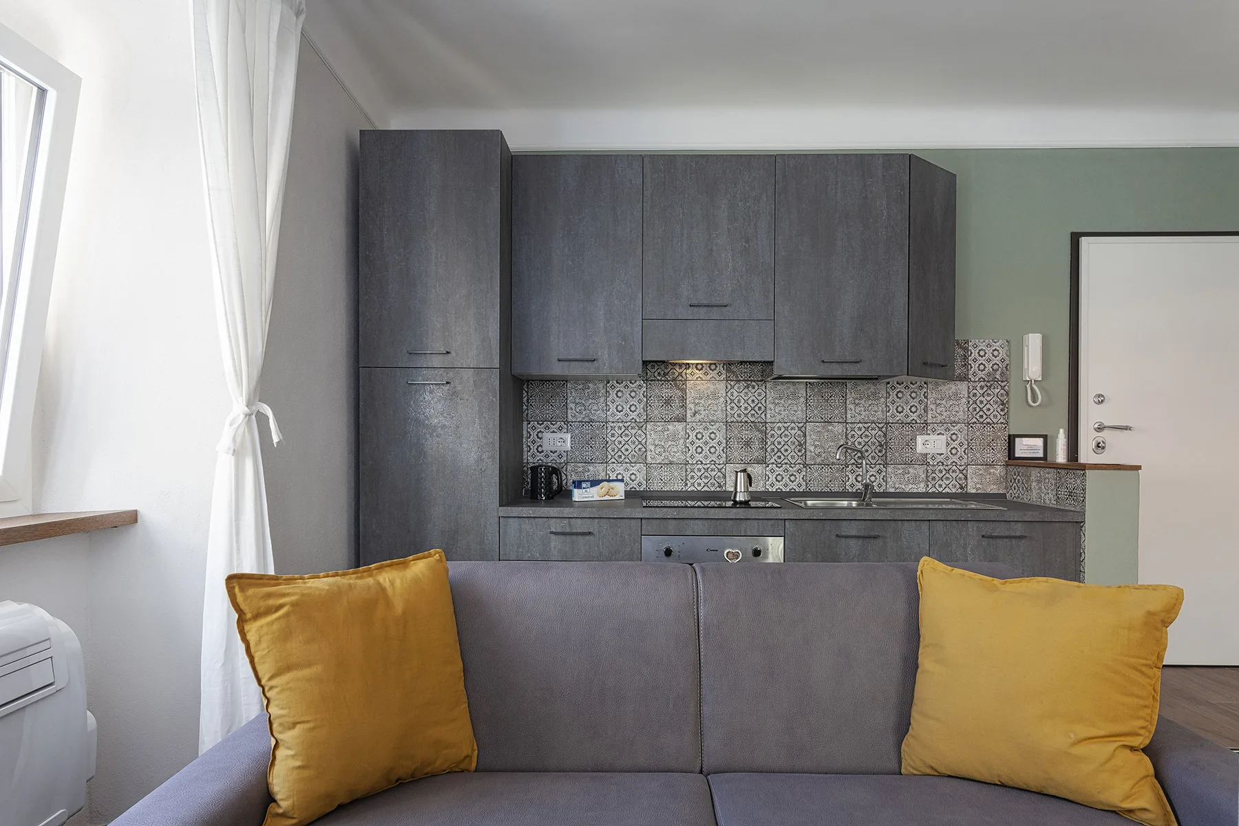 A living area faces a compact kitchen with dark cabinets and patterned tile.