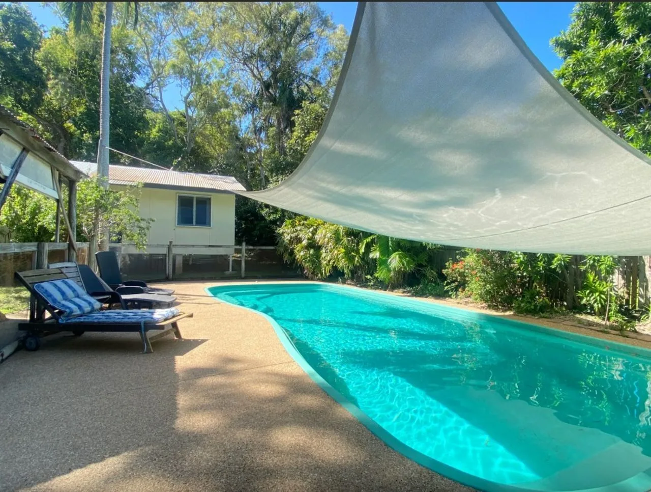 Una piscina al aire libre junto a asientos de descanso, bajo una gran lona de sombra.