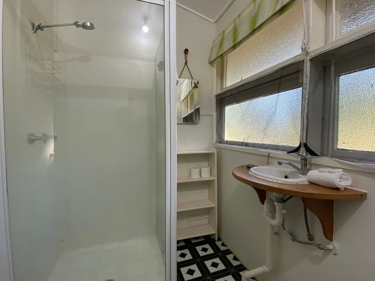 Un baño con una ducha de vidrio y un lavabo debajo de las ventanas.