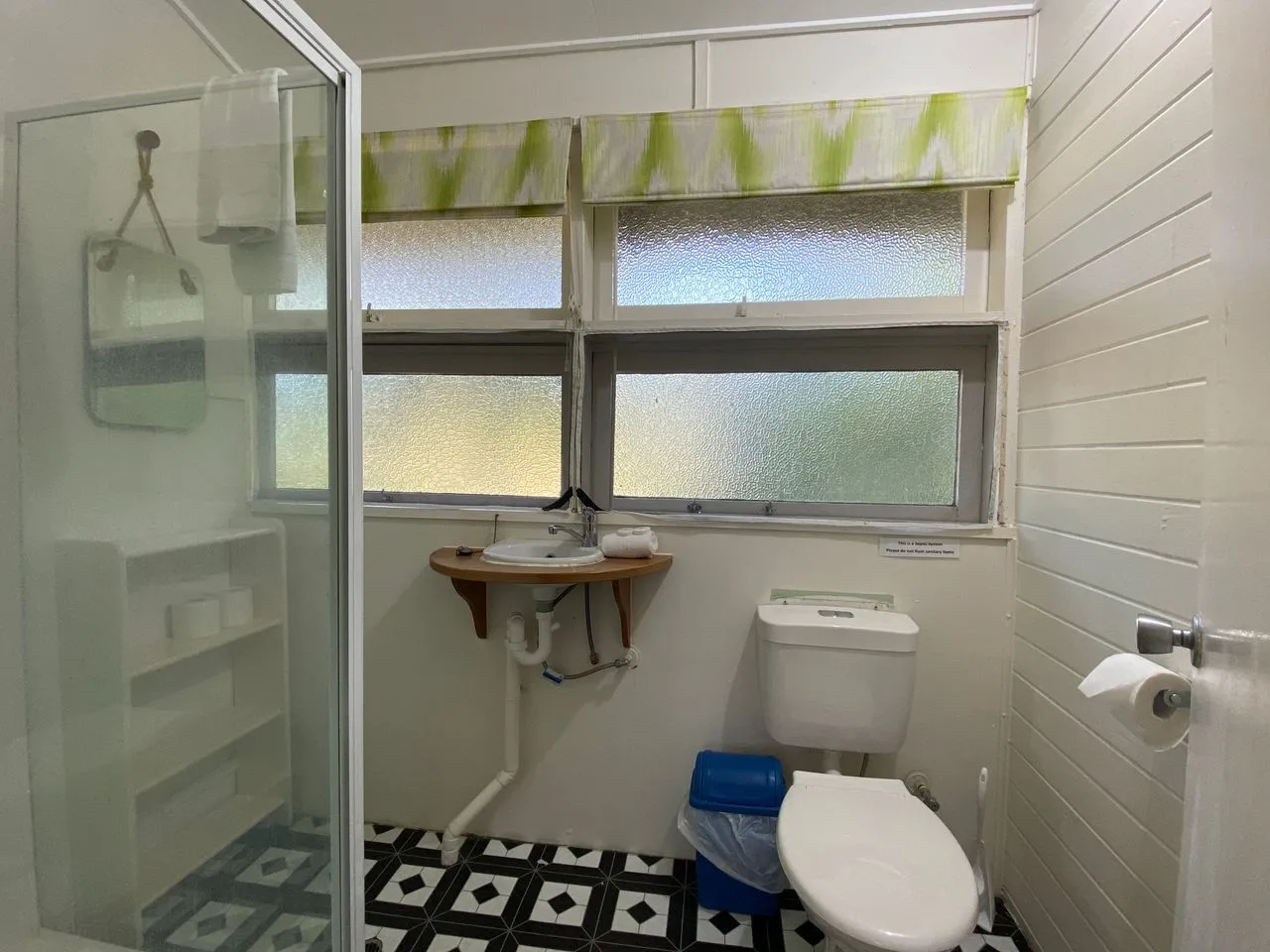 Un baño con ducha, lavabo e inodoro bajo ventanas esmeriladas.