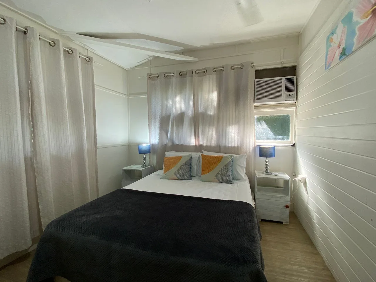 Dormitorio con una cama tendida, mesitas de noche y cortinas.