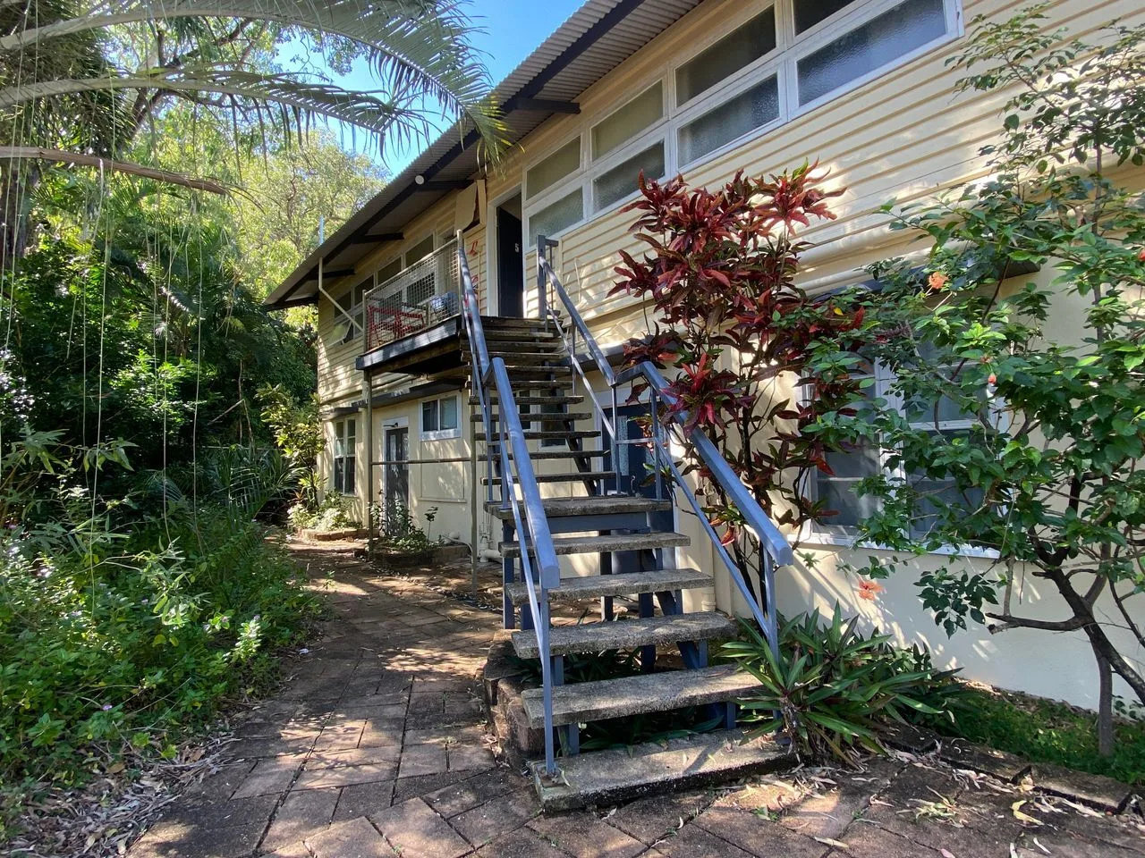 Exterior de un edificio elevado con una escalera exterior junto a plantas frondosas.