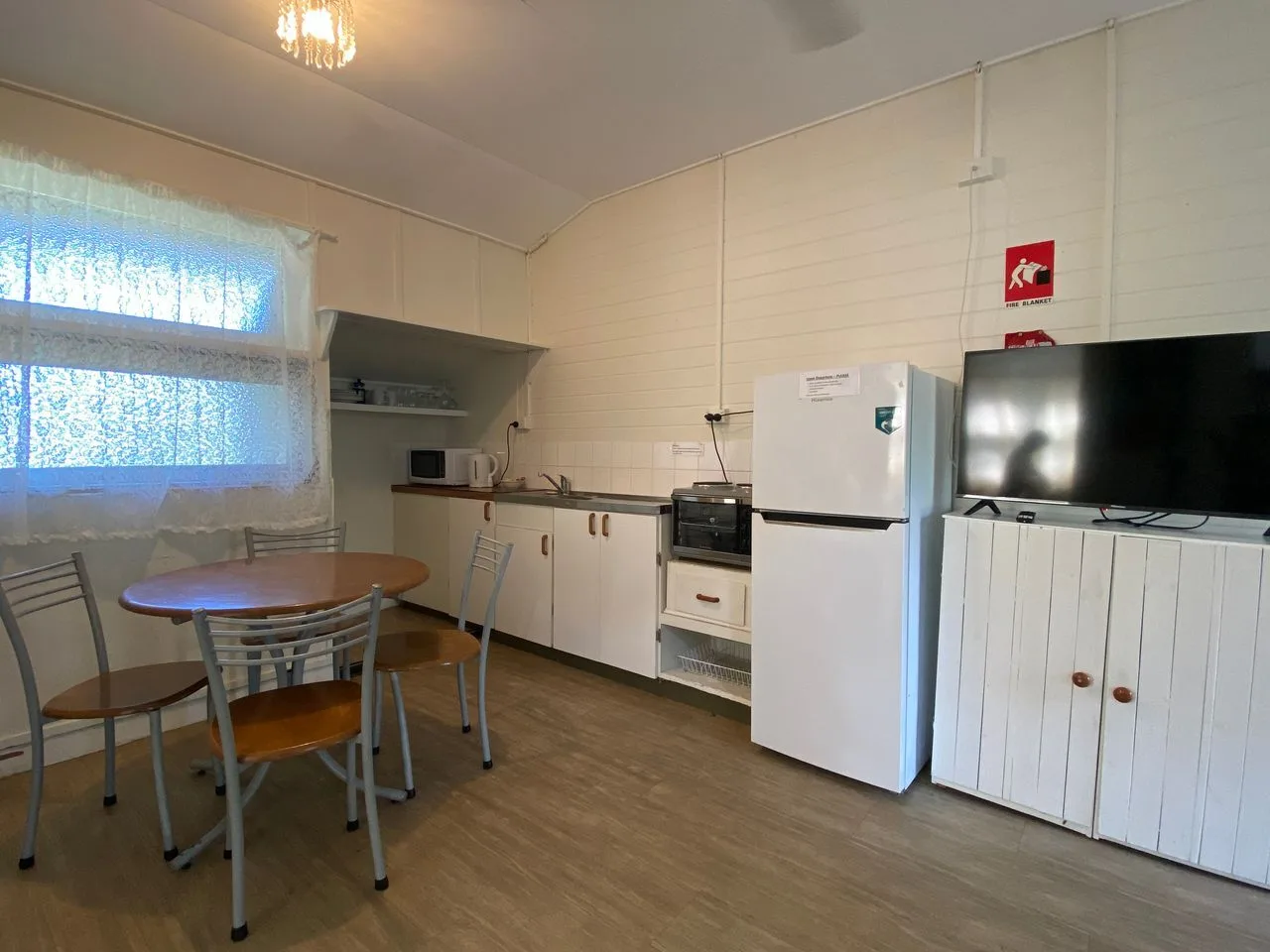 Una zona de cocina y comedor con mesa, asientos, electrodomésticos y televisor.