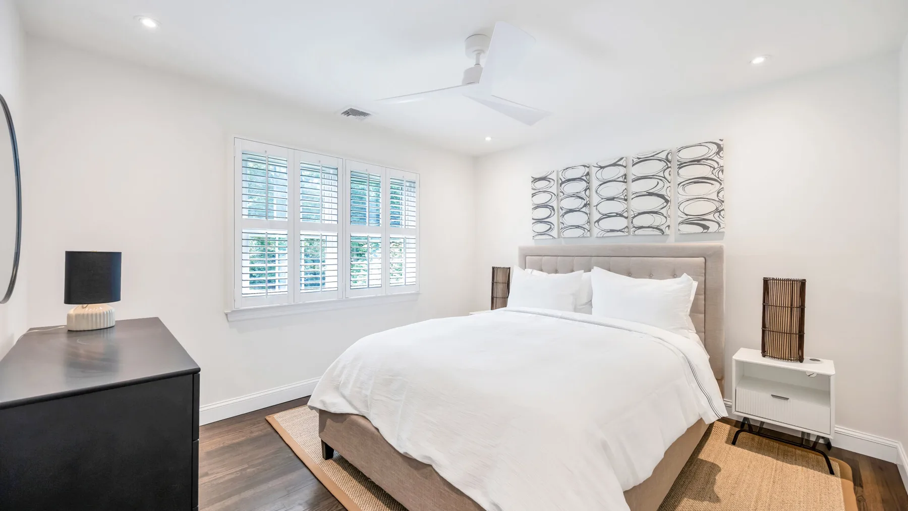 Un dormitorio luminoso con una cama tendida y ventanas con contraventanas.
