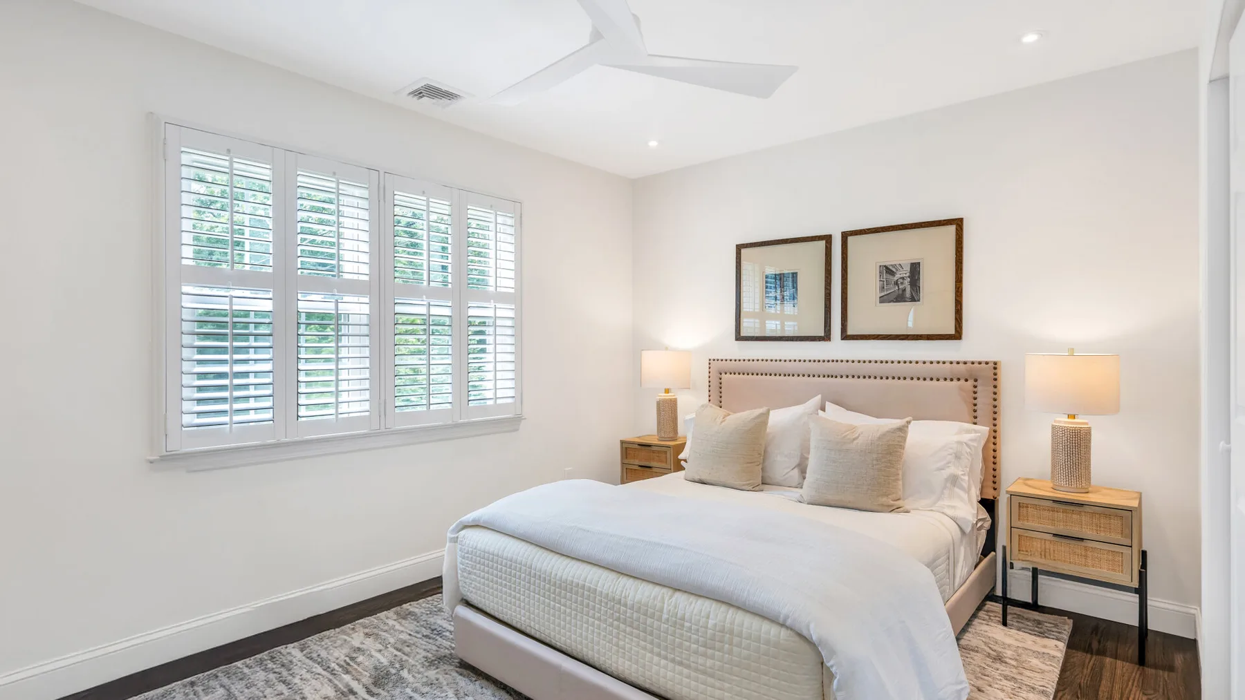 Un dormitorio luminoso con una cama bien tendida y ventanas con contraventanas.