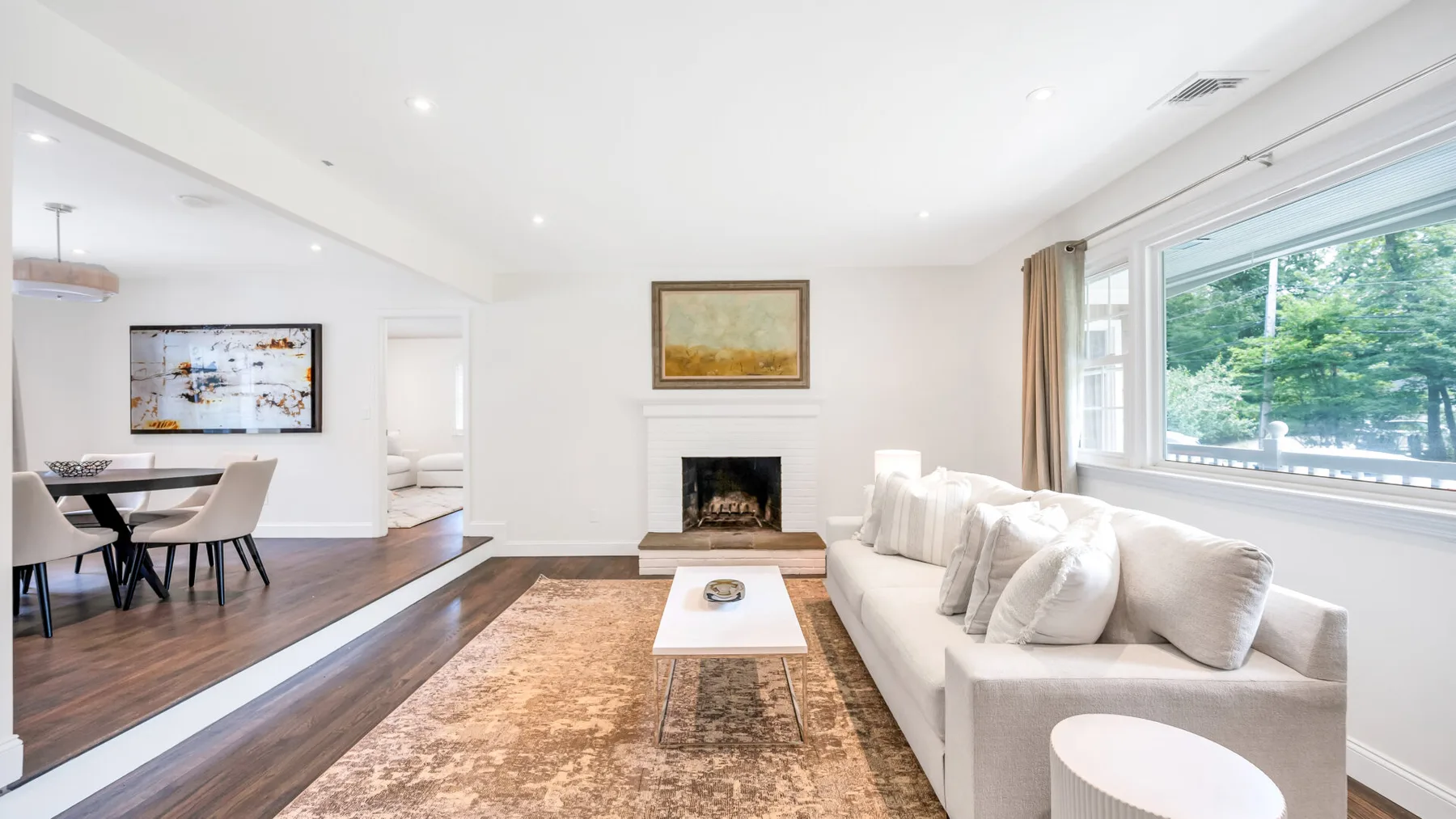 A bright living room with a white seating area, fireplace, and large window.