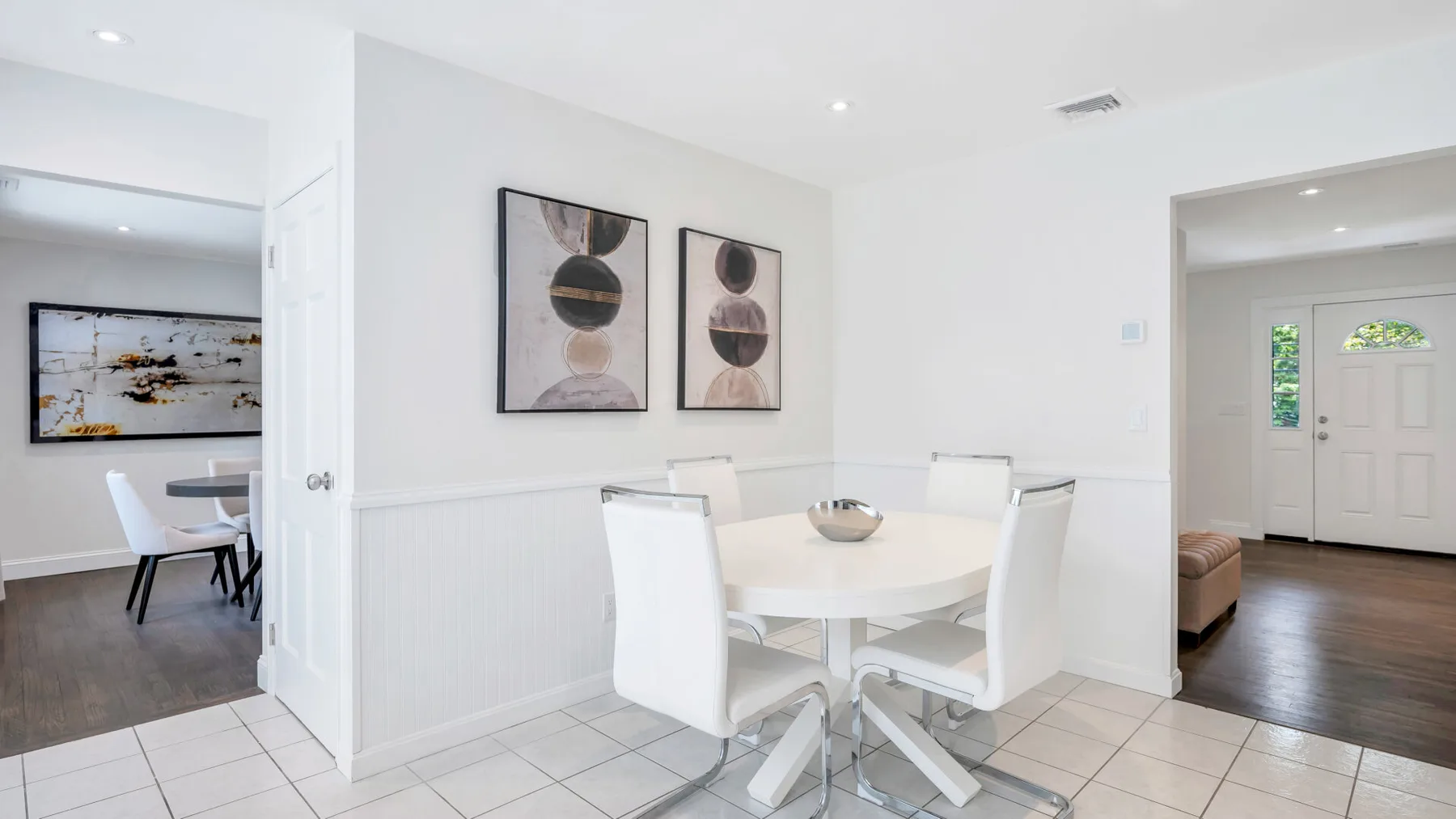 Un comedor luminoso con una mesa redonda y asientos blancos junto a una puerta abierta.