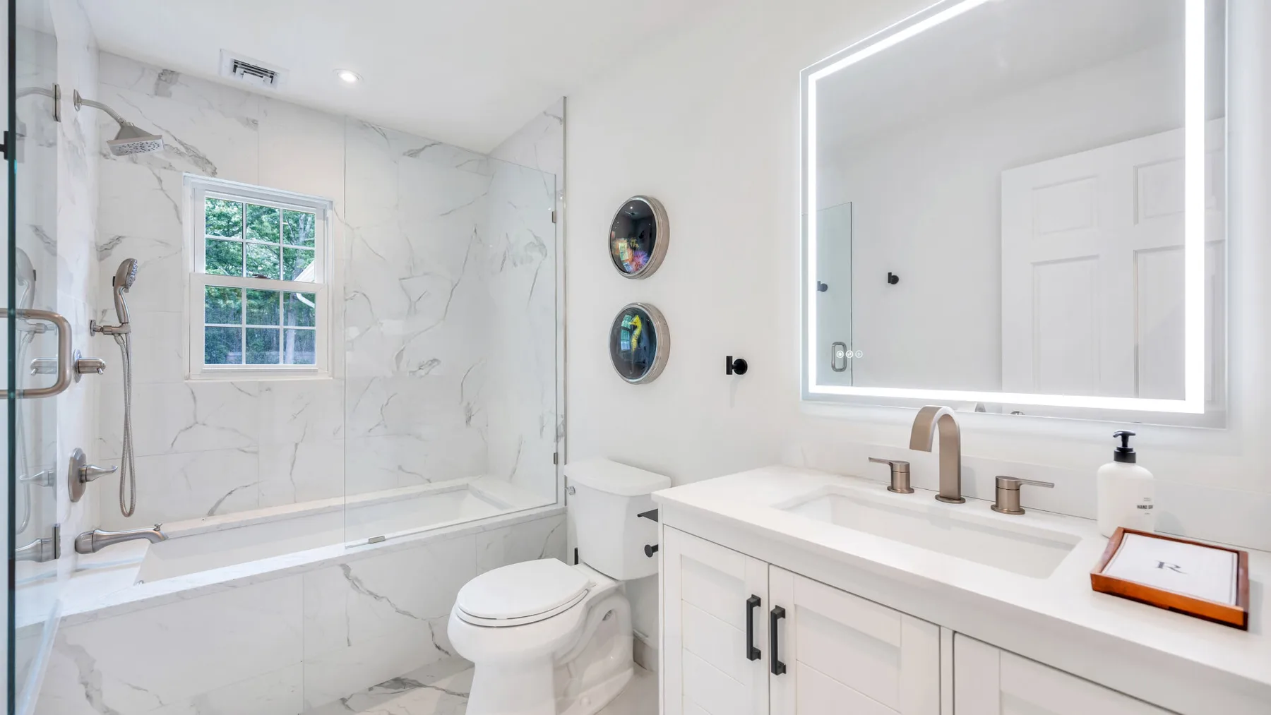 Un baño luminoso con bañera, inodoro y tocador bajo un espejo grande.