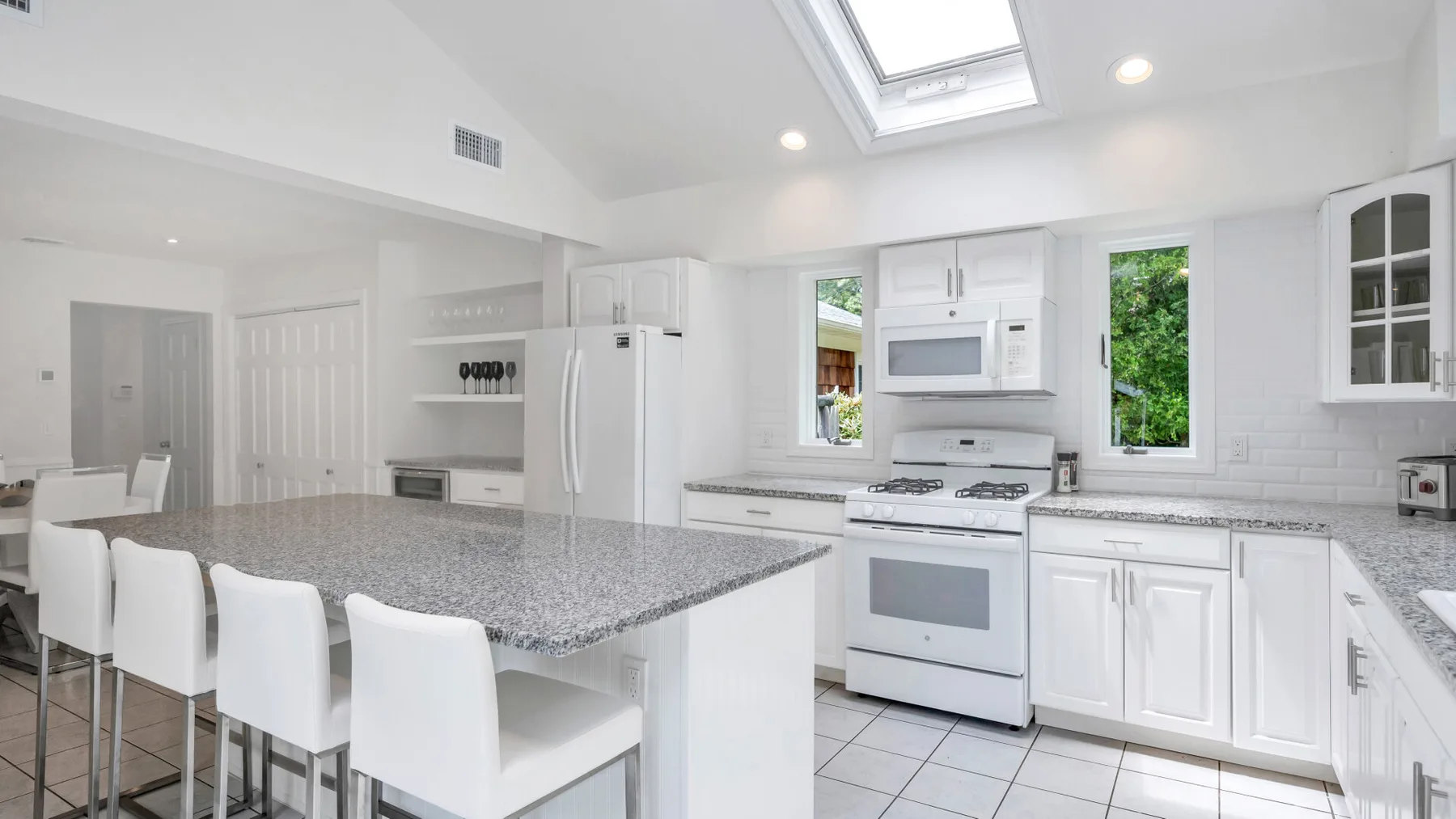 Una cocina blanca y luminosa con una isla grande y electrodomésticos de acero inoxidable.