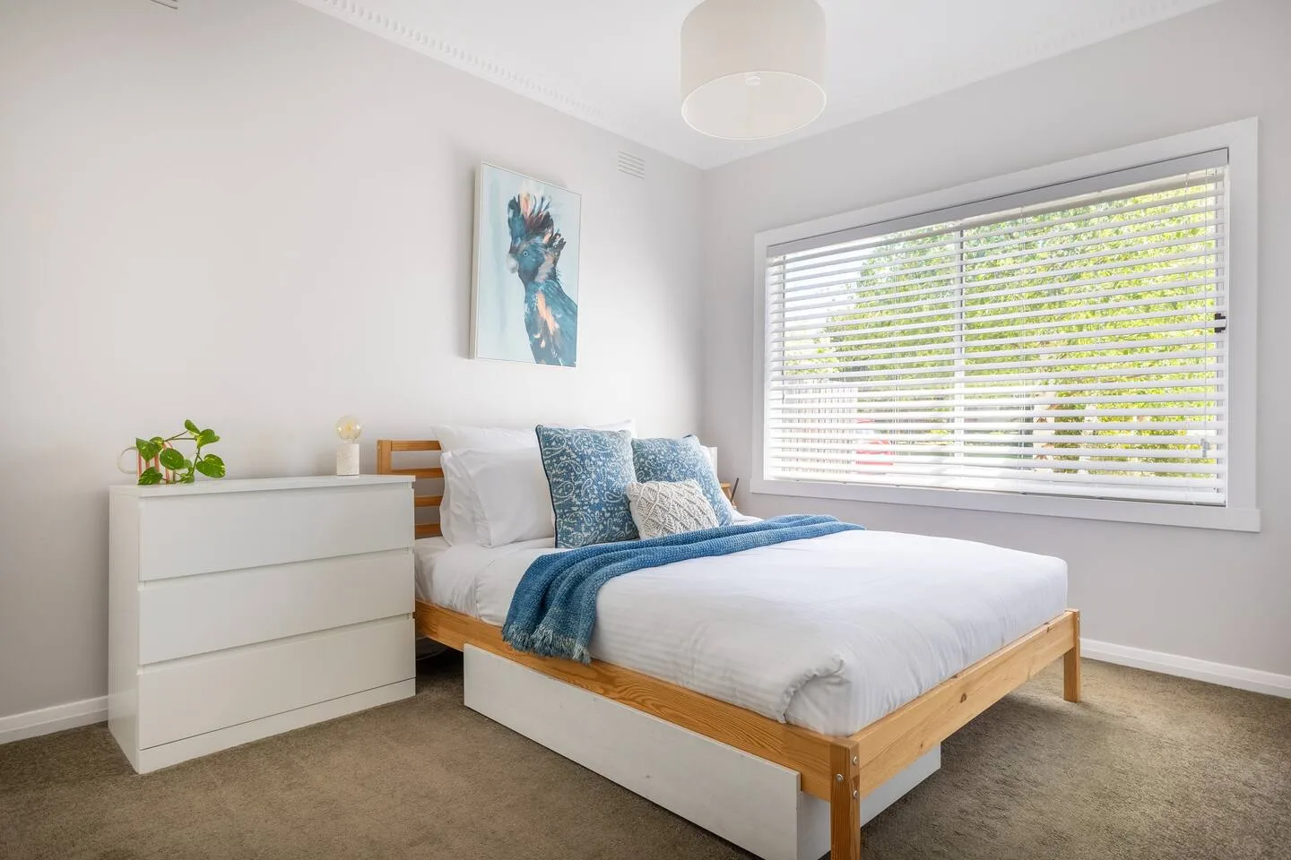 Un dormitorio con una cama vestida con ropa de cama blanca y azul junto a una ventana.