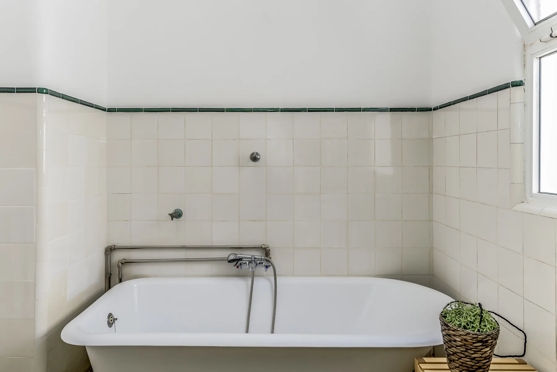Un baño con bañera bajo paredes alicatadas y una ventana pequeña.