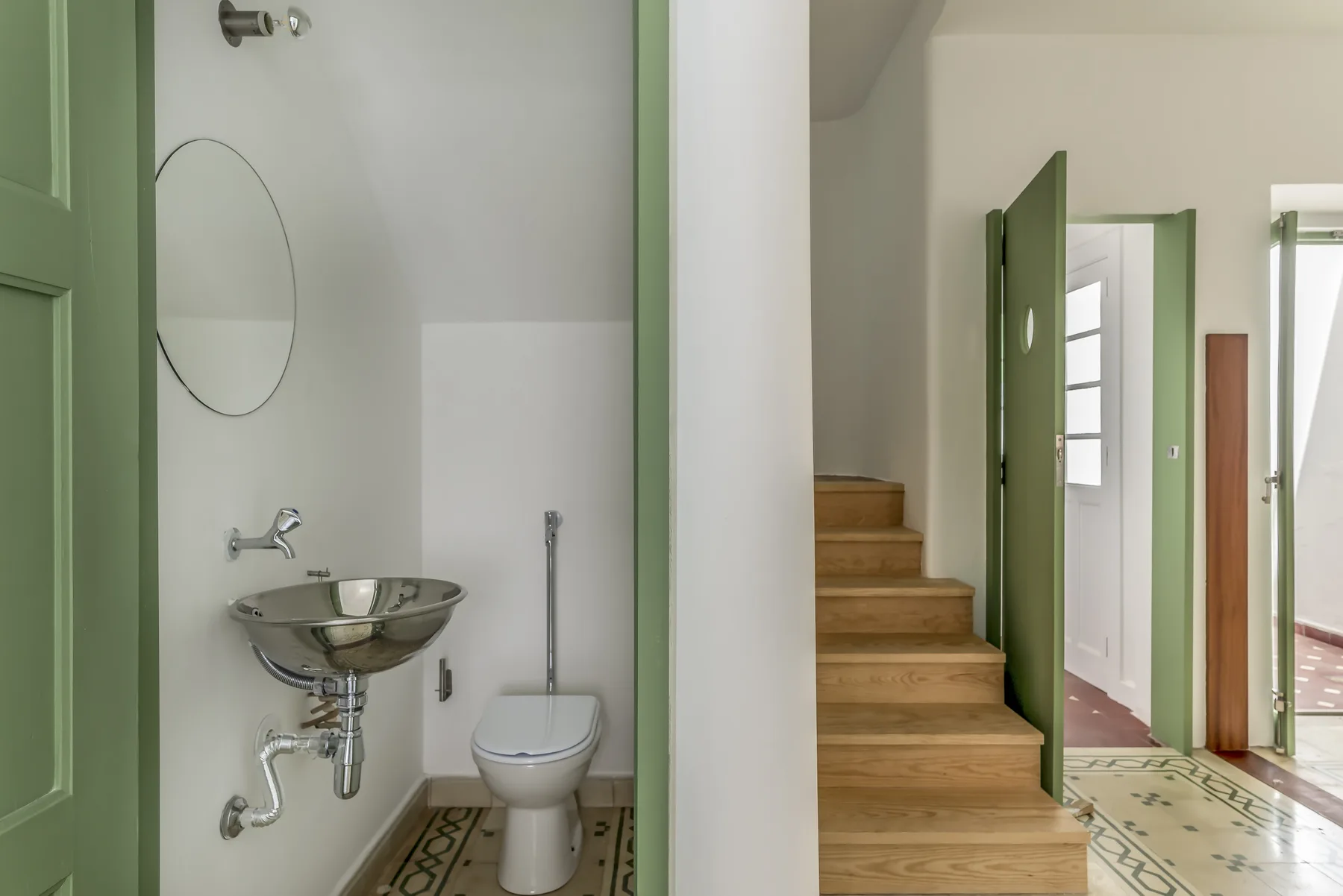 Un baño con lavabo e inodoro junto a una escalera de madera.