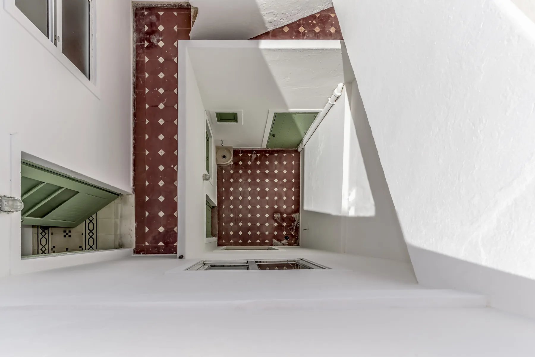 Una escalera interior abierta con paredes blancas y suelo de azulejos estampados.