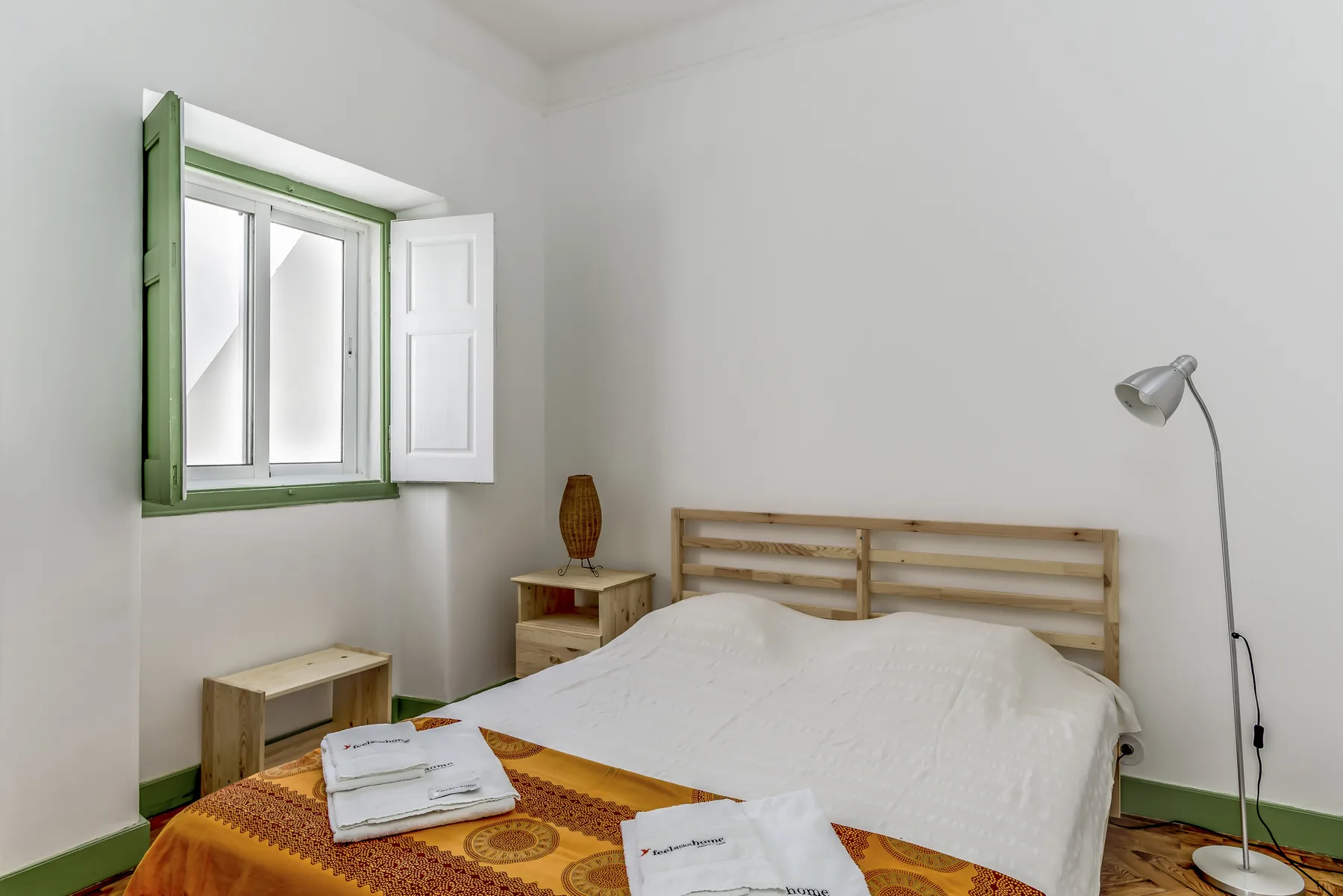 Un dormitorio con una cama, una ventana con marco verde y una mesita de noche.