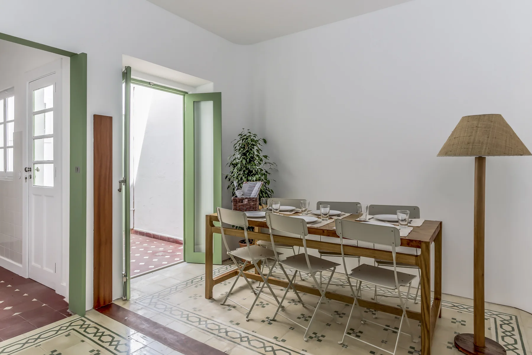 Comedor con una mesa larga y sillas junto a una puerta verde abierta.