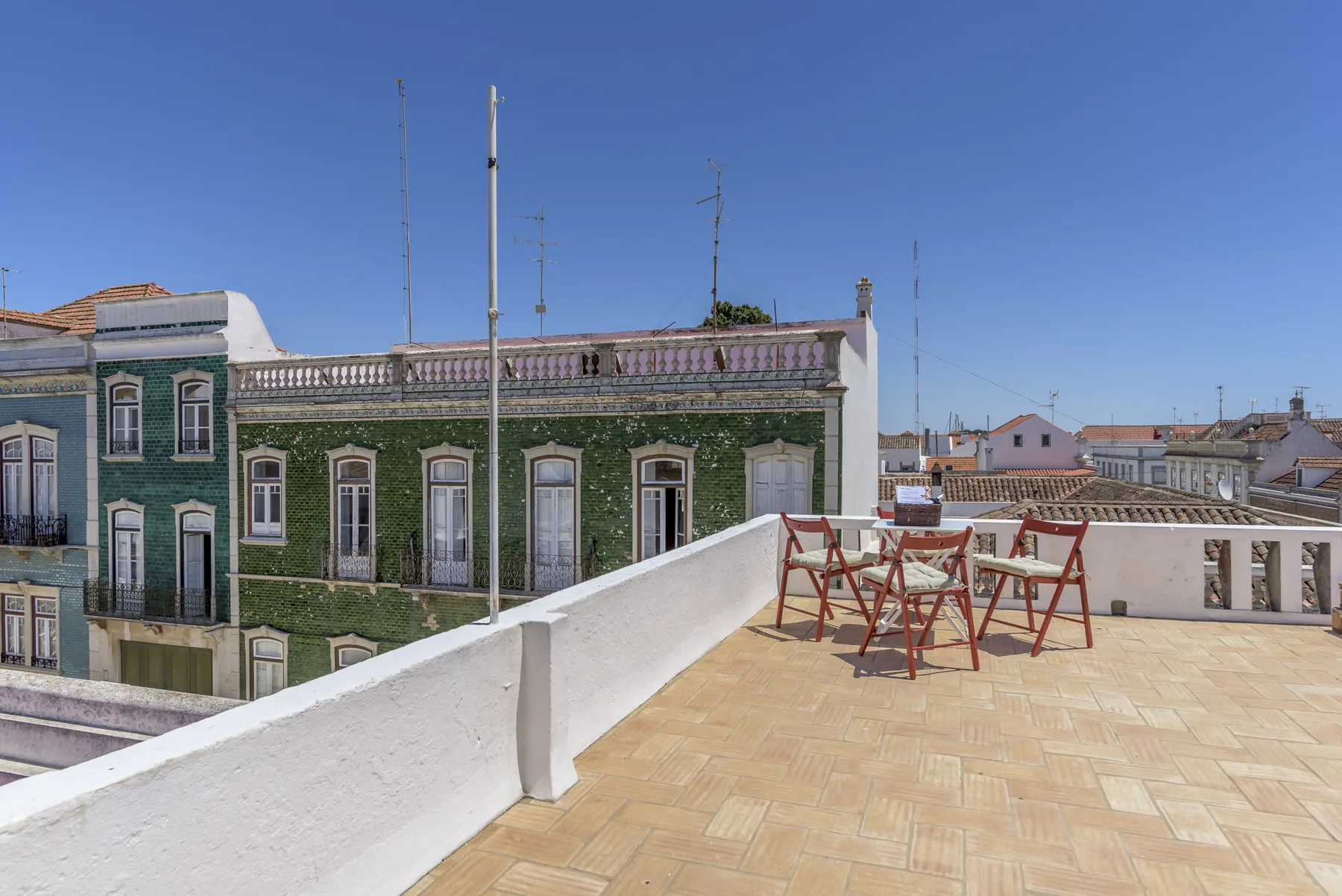 Una terraza en la azotea con suelo de baldosas, mesas al aire libre y tejados alrededor.