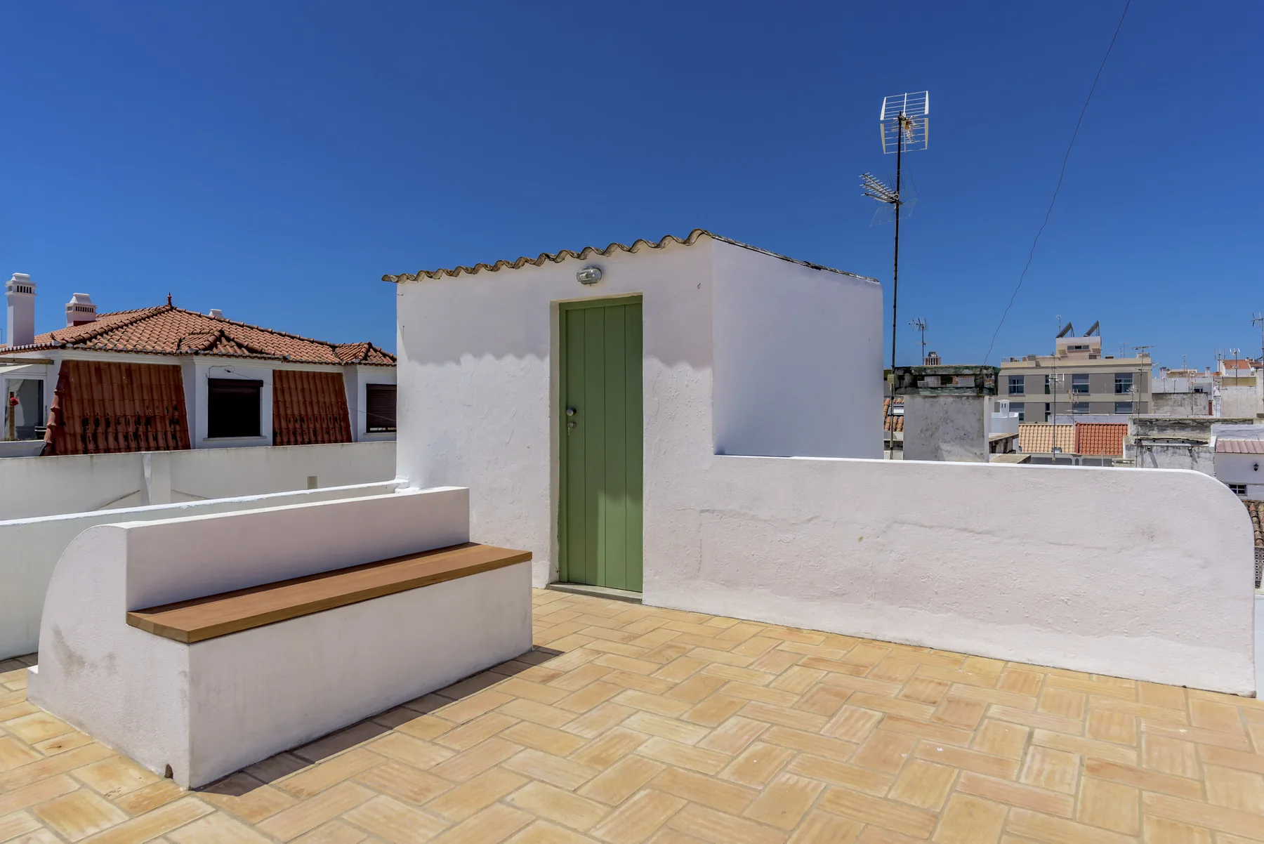 Una terraza soleada en la azotea con una puerta verde y asientos integrados.