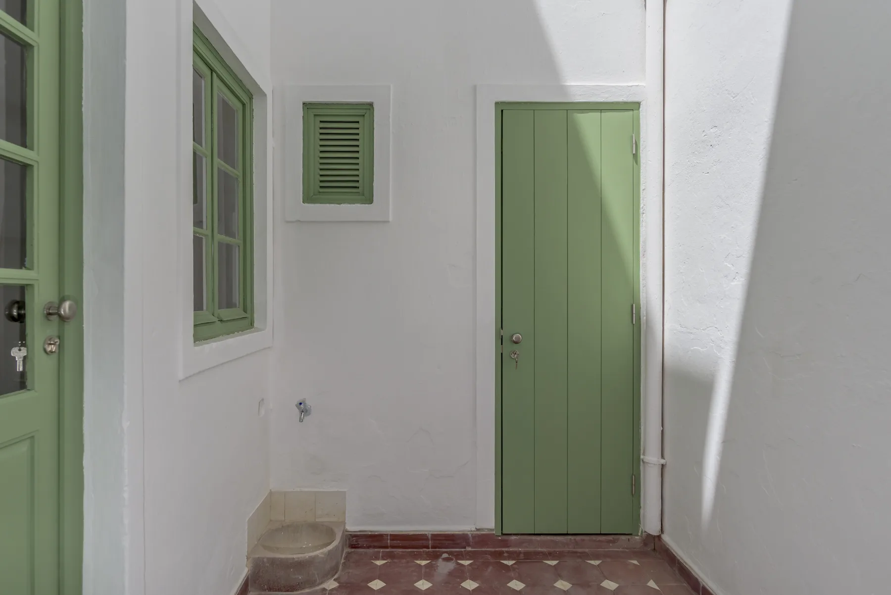 Un pequeño recibidor con puertas verdes y suelo de baldosas estampadas.