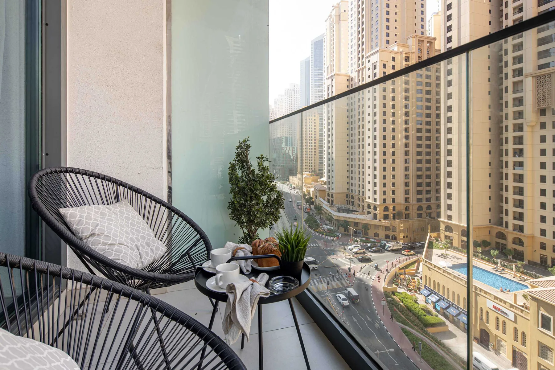 A balcony seating area overlooks a street and surrounding high-rise buildings.