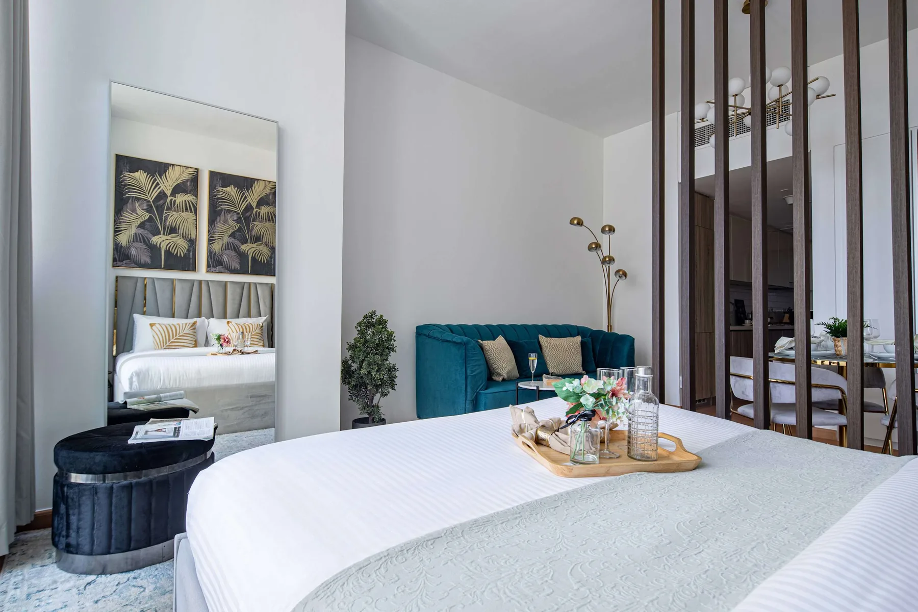 A bright bedroom with a large bed, teal seating, and a mirrored wall panel.