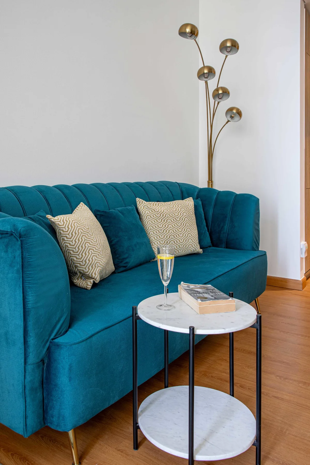 A teal sofa with patterned cushions sits beside a small round table in a living room.