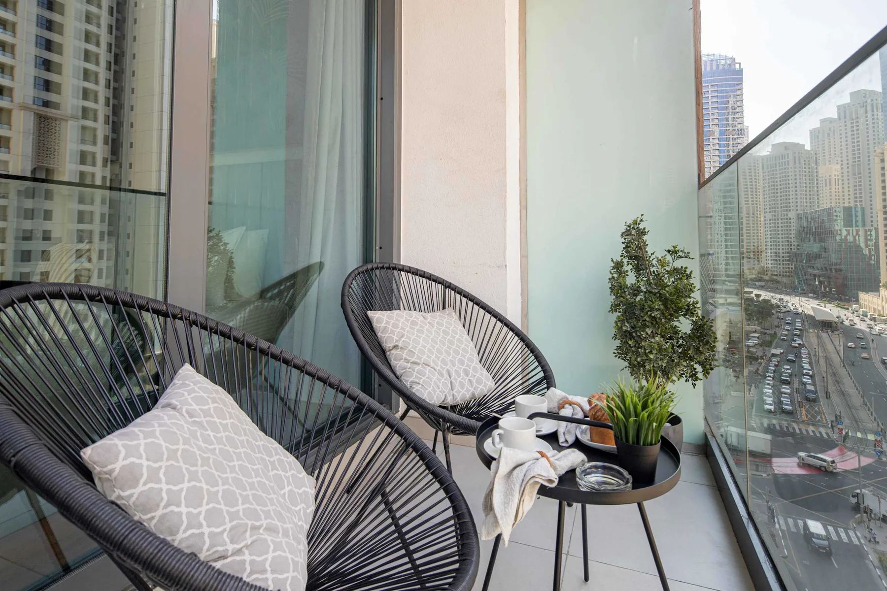 A balcony seating area with two woven chairs, plants, and views of nearby buildings.