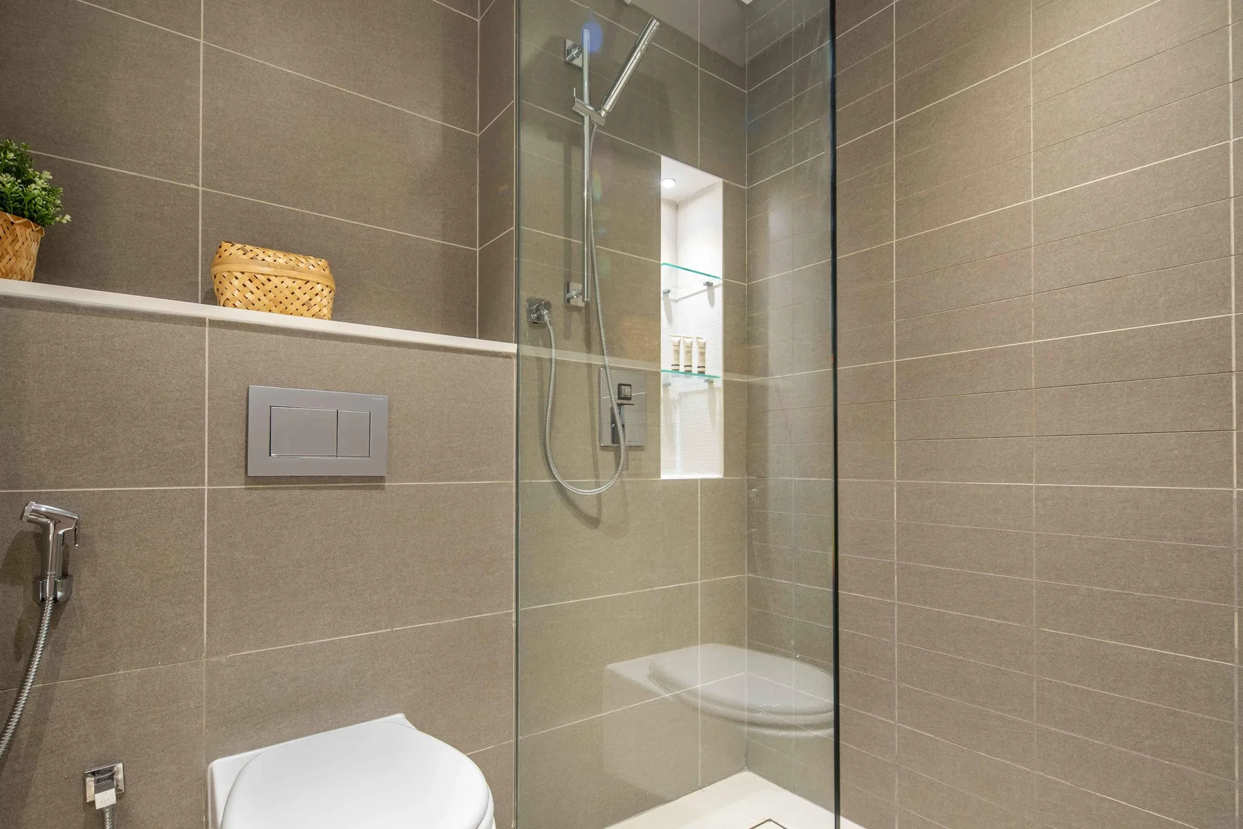 A tiled bathroom with a glass shower and a wall-mounted toilet.