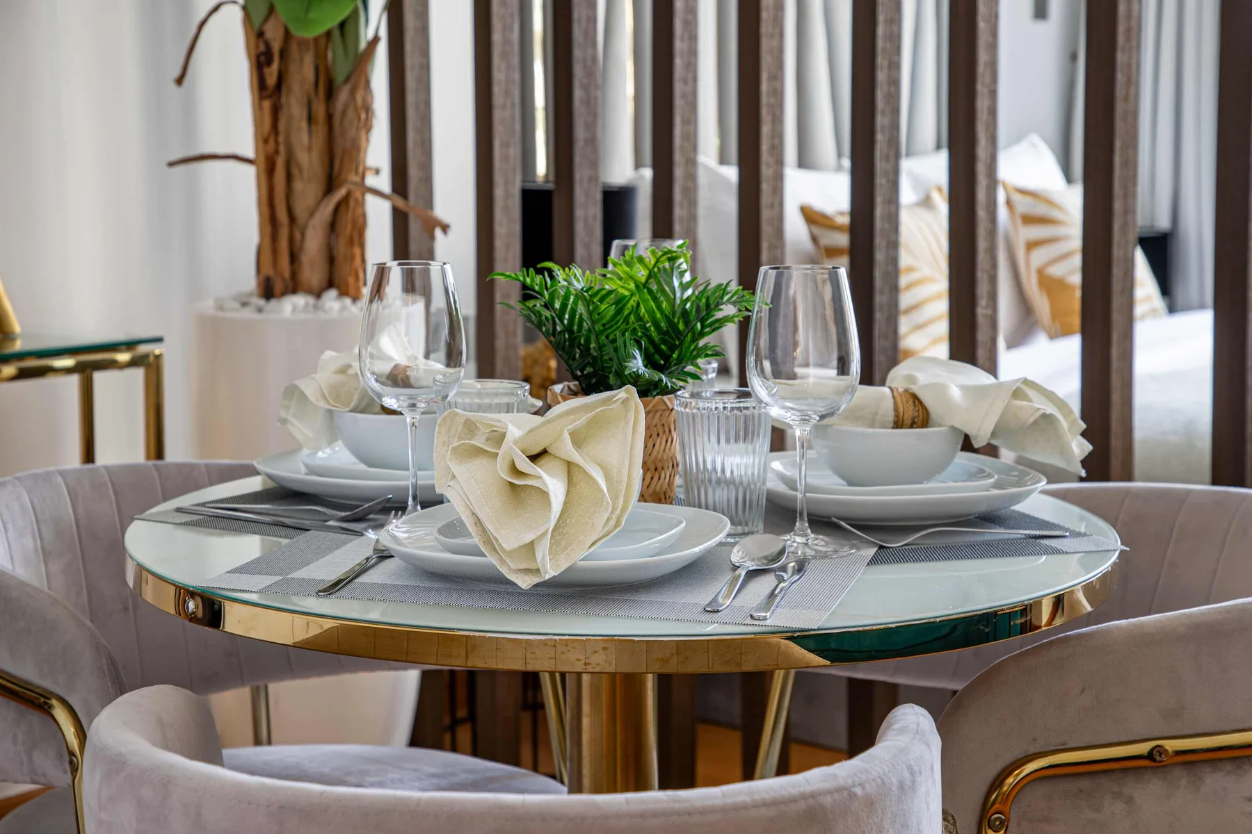 A dining table is set with plates, glasses, folded napkins, and a small plant.