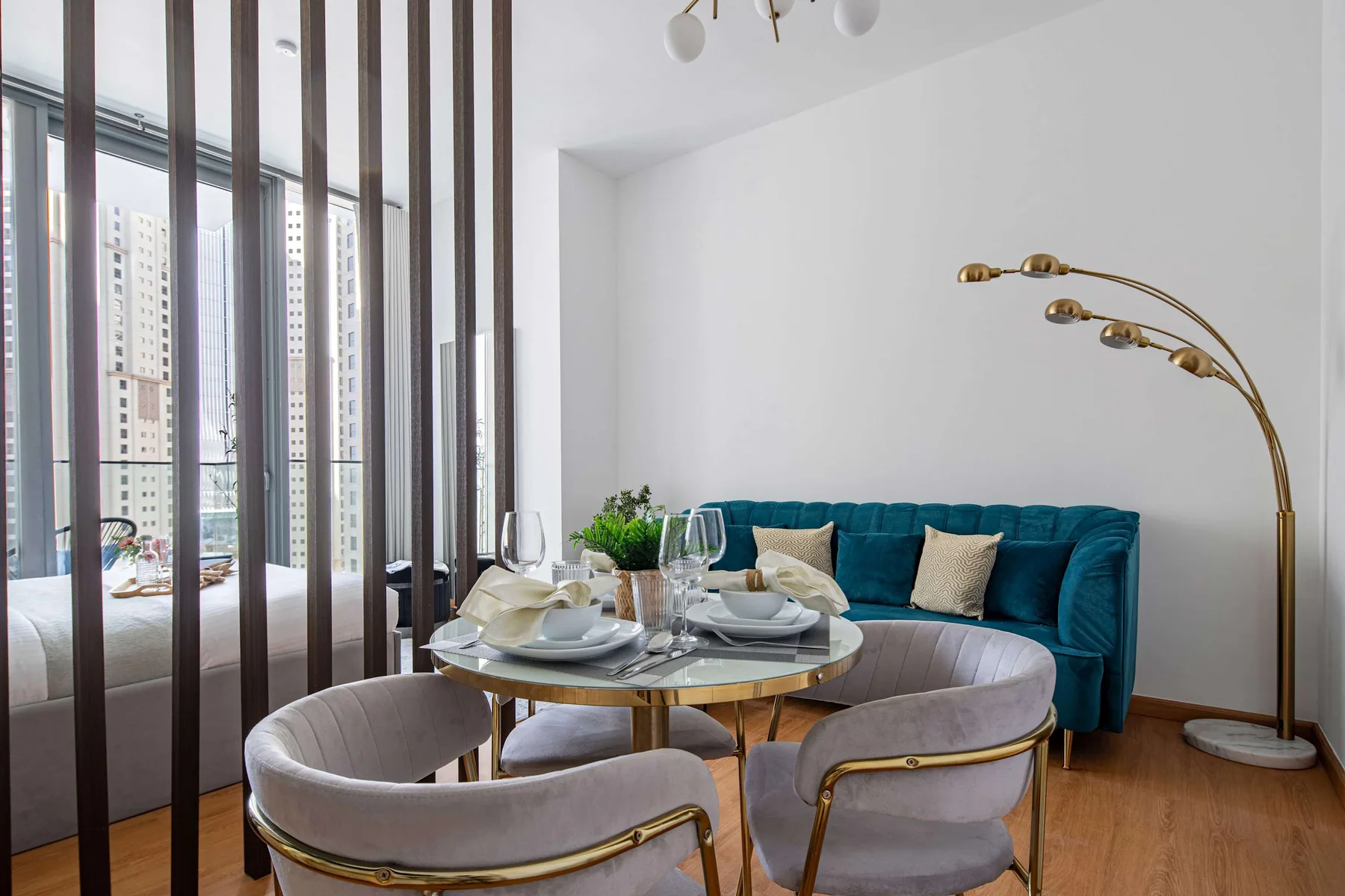 A dining area with a round table and seating beside a teal sofa.