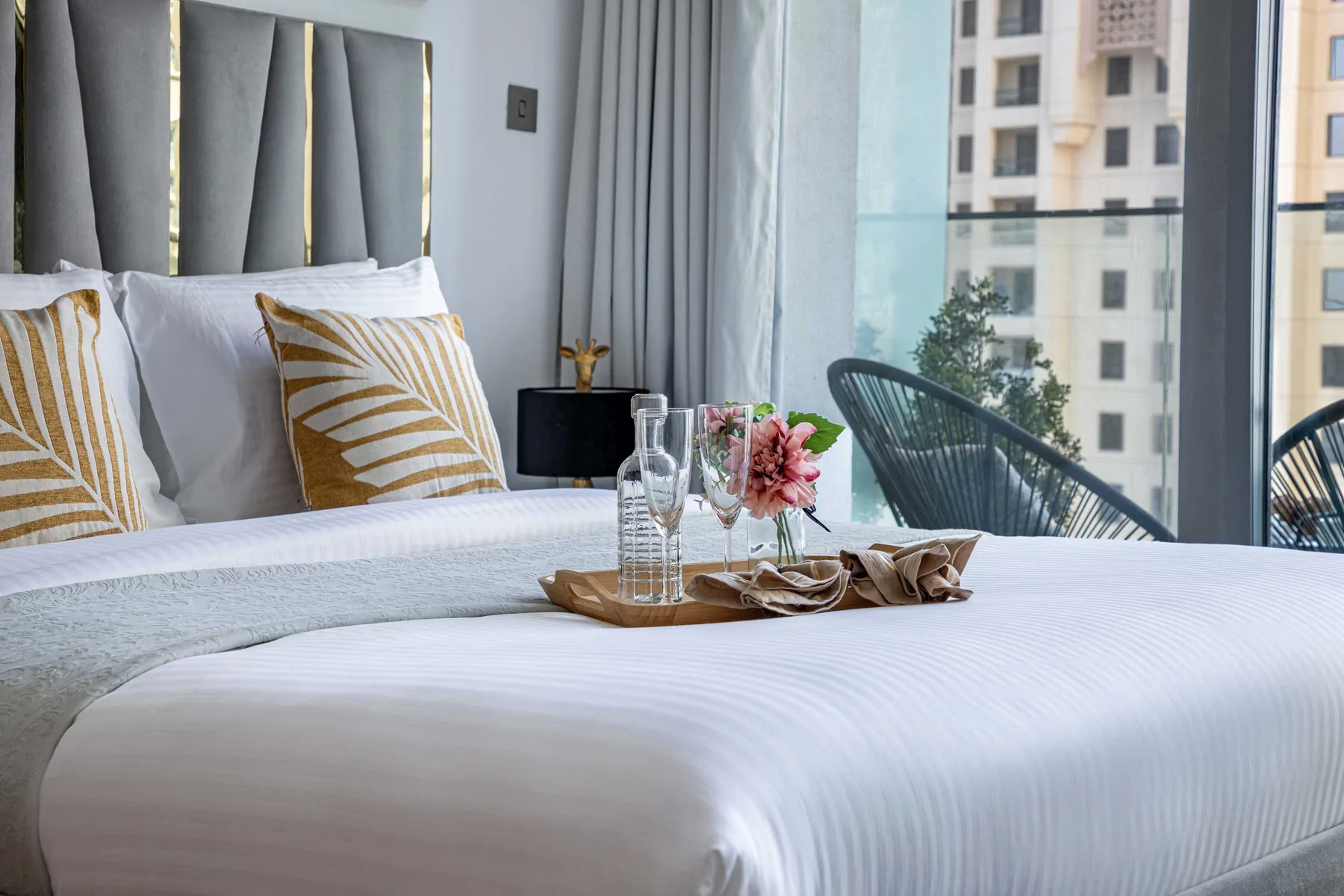 A neatly made bedroom with patterned pillows and a tray of flowers on the bed.