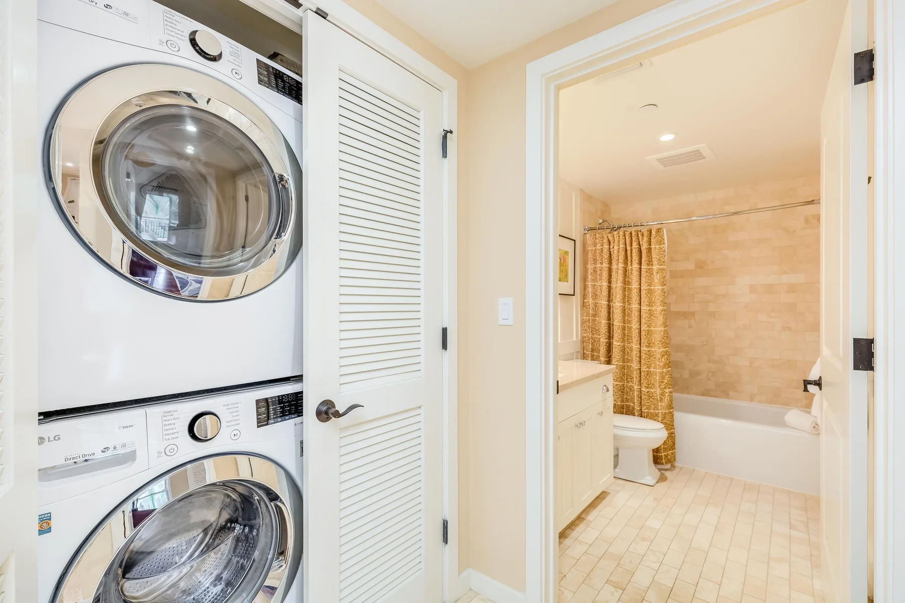 A laundry area beside a bathroom with a bathtub and shower curtain.