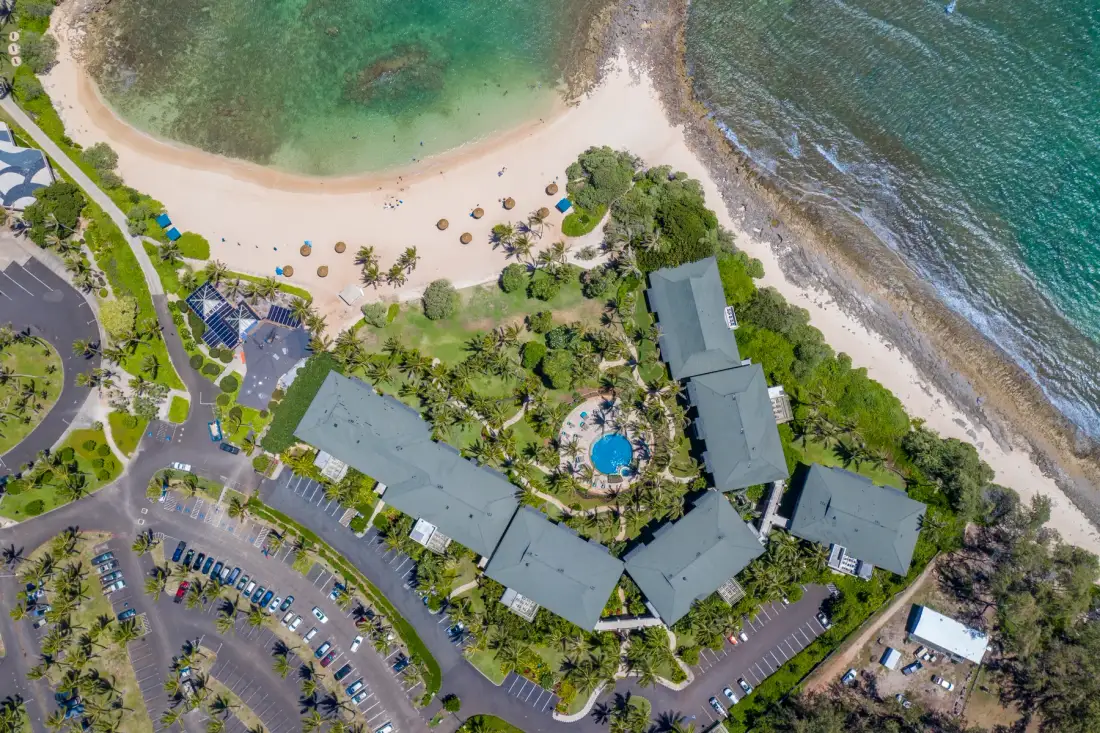 An aerial view of a beachfront resort with buildings, gardens, and a sandy shoreline.