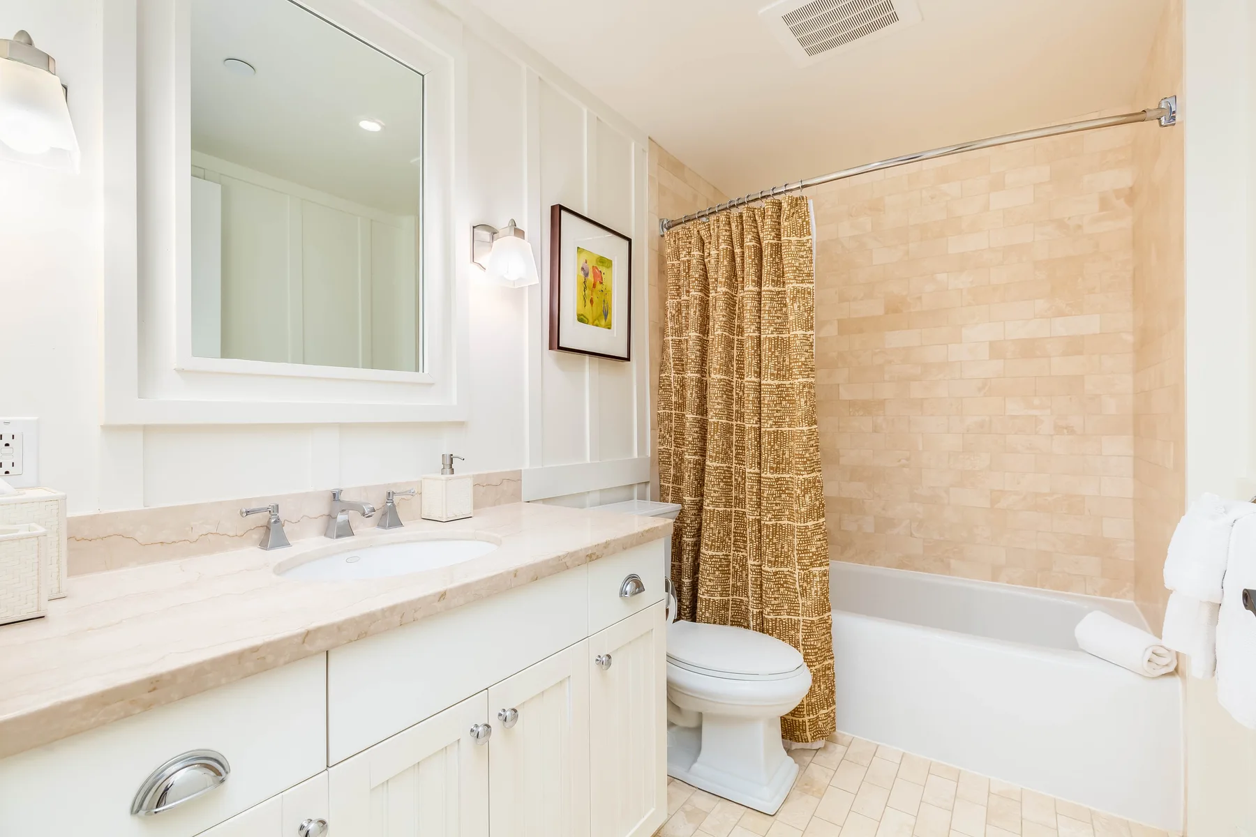 A bright bathroom has a long vanity, a bathtub, and a patterned shower curtain.