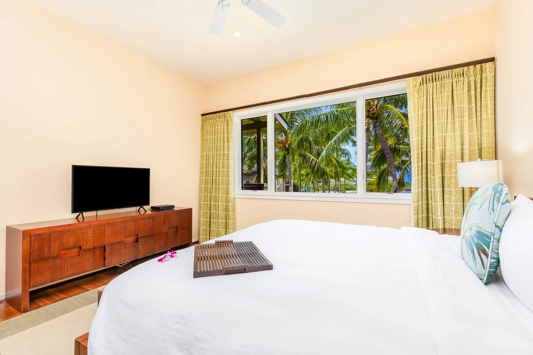 A bedroom with a bed, television, and a window overlooking palm trees.