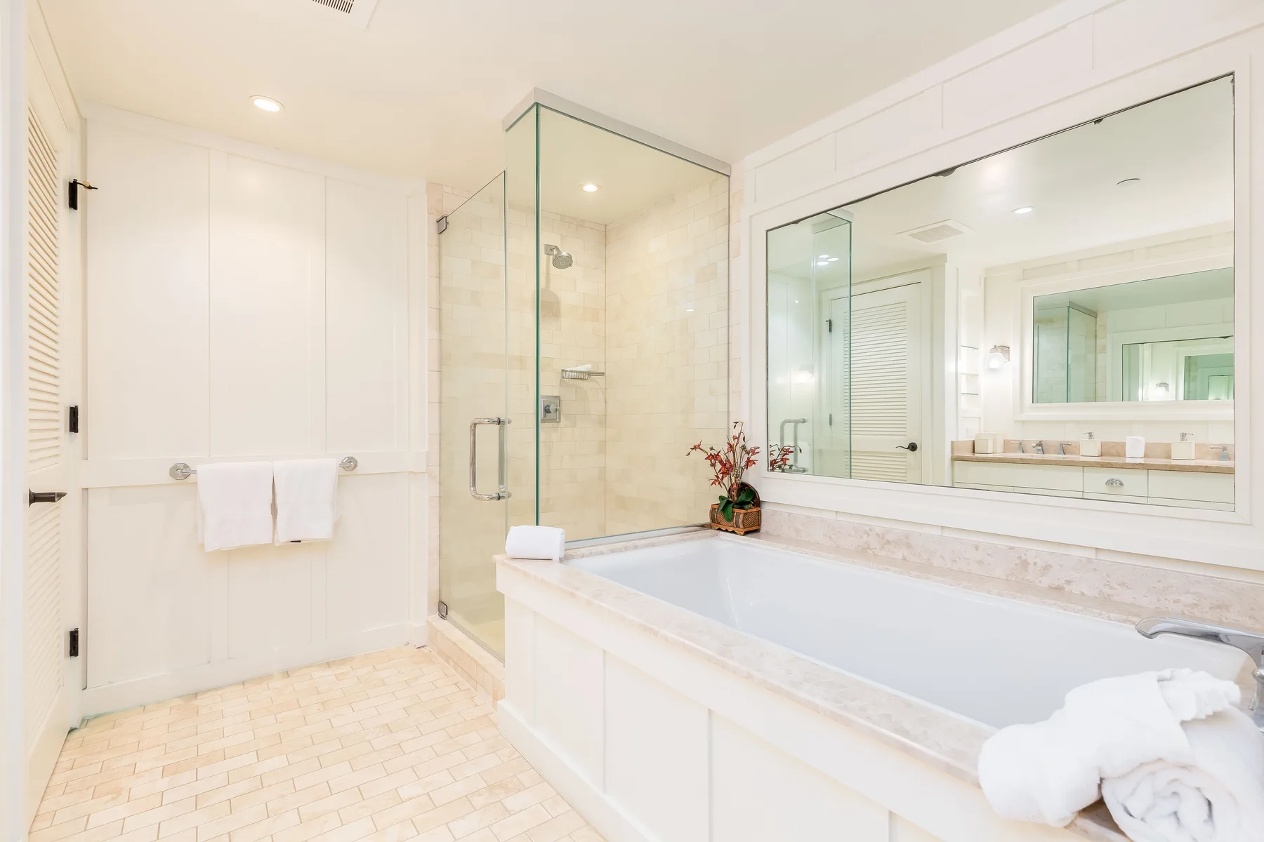 A bright bathroom with a bathtub, glass shower, and large mirror.