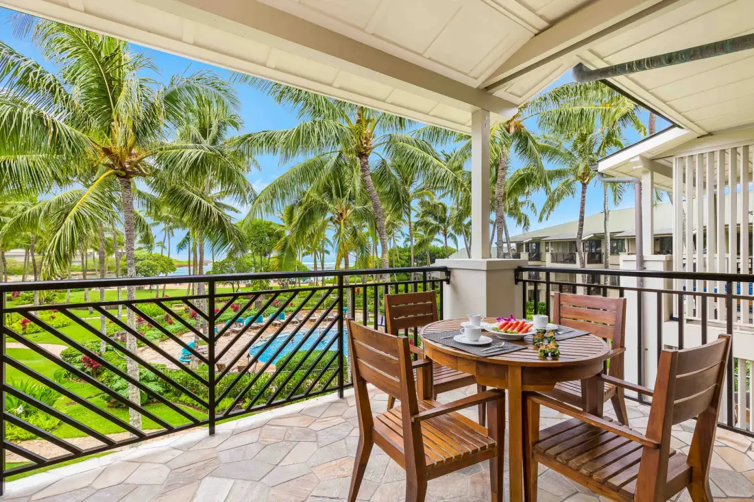 Un comedor exterior cubierto tiene vistas a una piscina y palmeras.