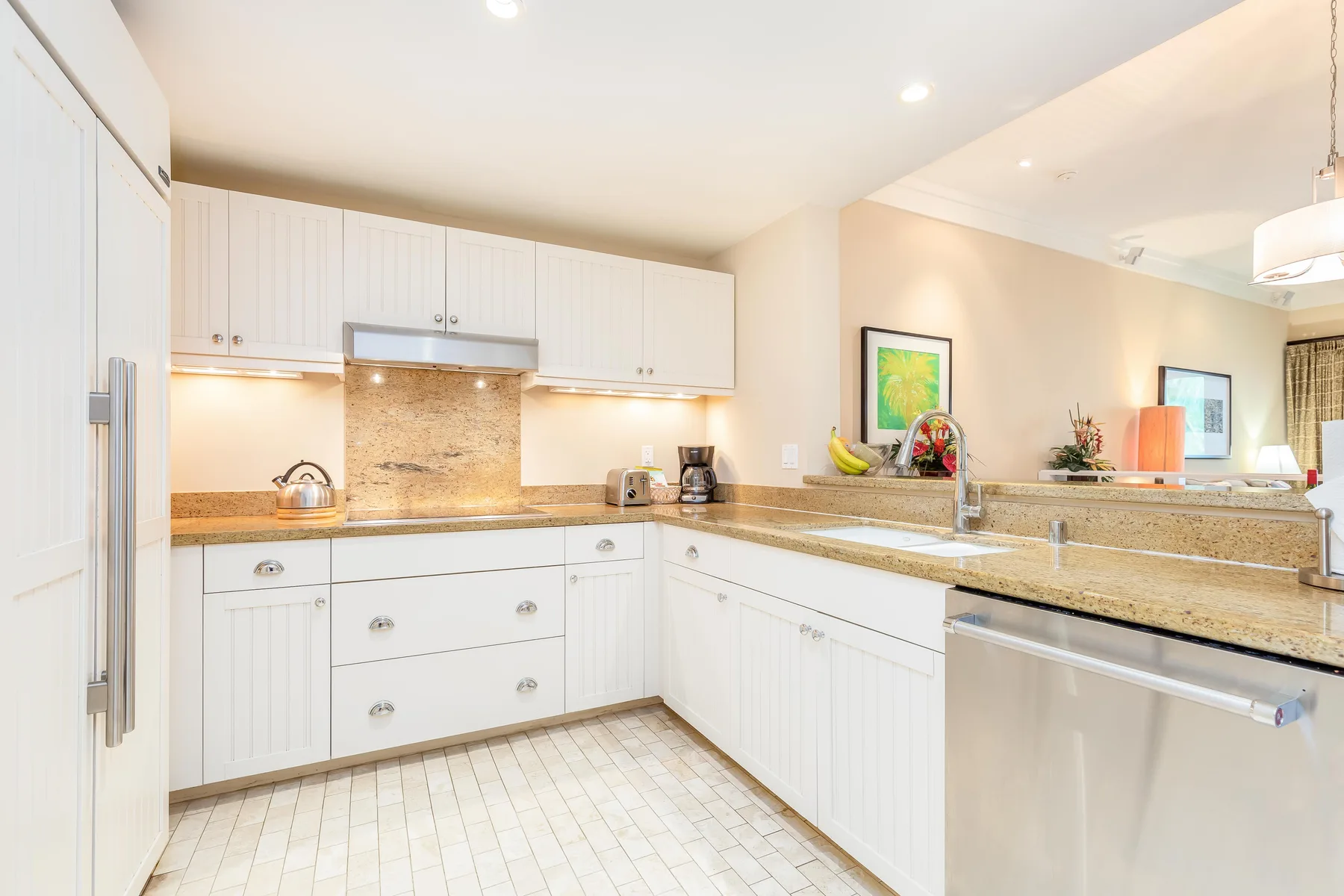 A bright kitchen with white cabinets, stone counters, and a sink.