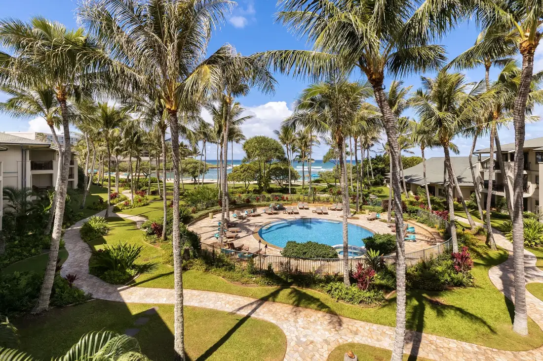 A landscaped tropical courtyard surrounds a pool, with palm trees and the ocean beyond.