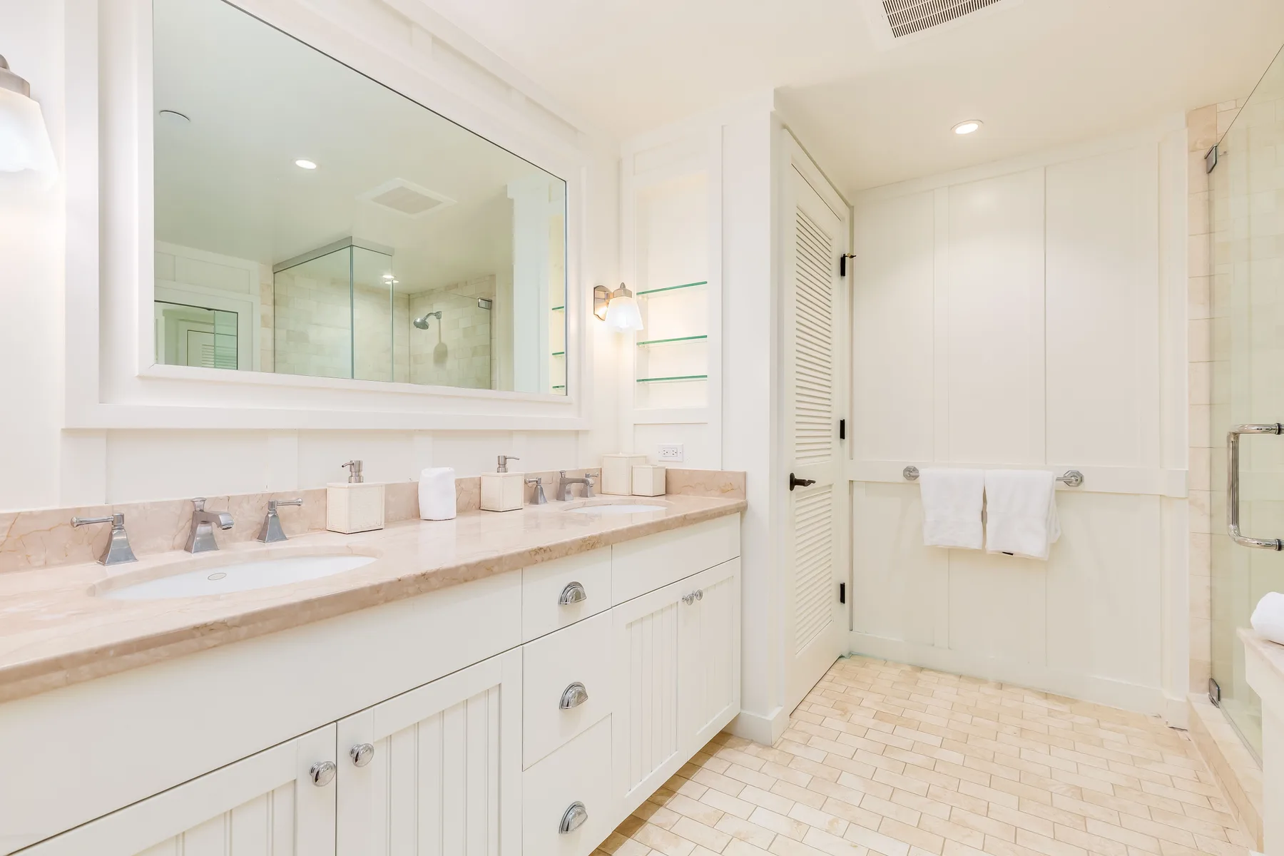 A bright bathroom with a long vanity, large mirror, and glass shower.