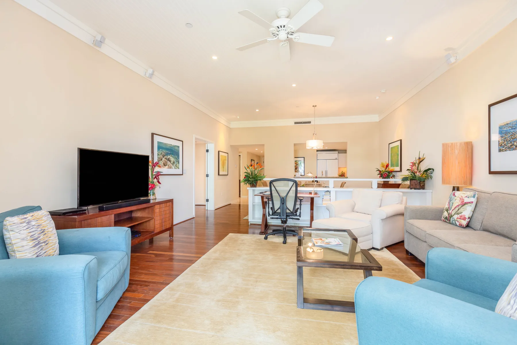 A bright living room with seating, a television, and a dining area beyond.
